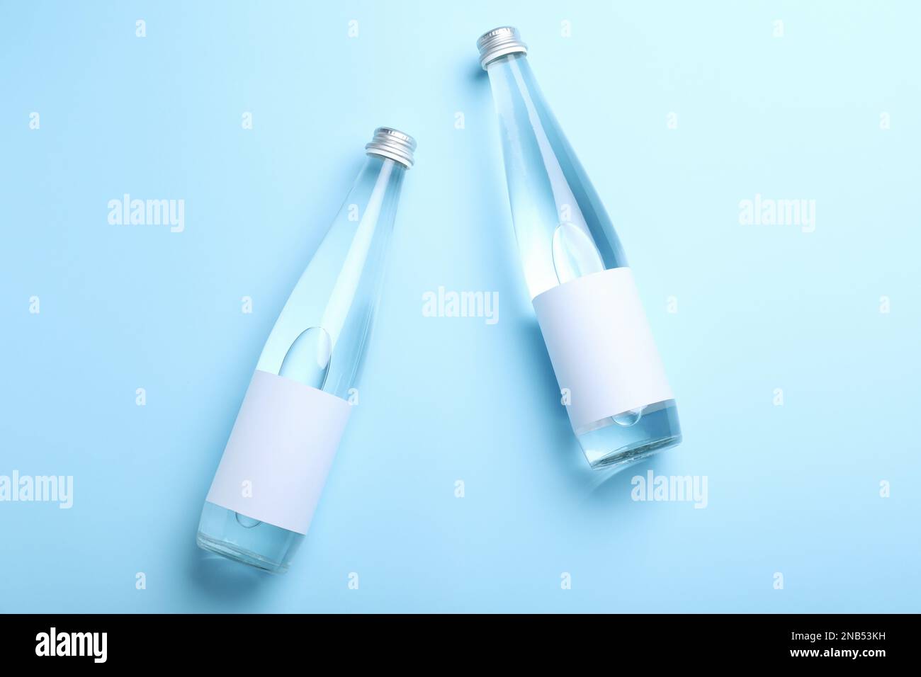 Glass bottles of water with blank label on light blue background, flat lay Stock Photo Alamy