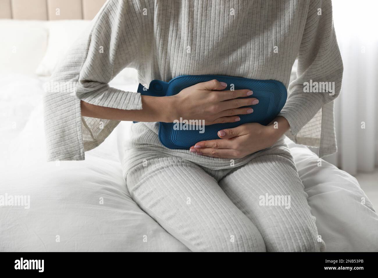 Woman using hot water bottle to relieve abdominal pain on bed at home, closeup Stock Photo