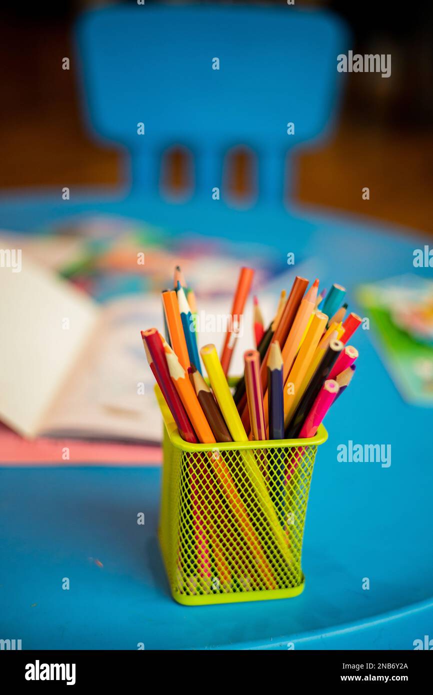 A yellow container with many colored pencils is placed on a blue children's table, next to some