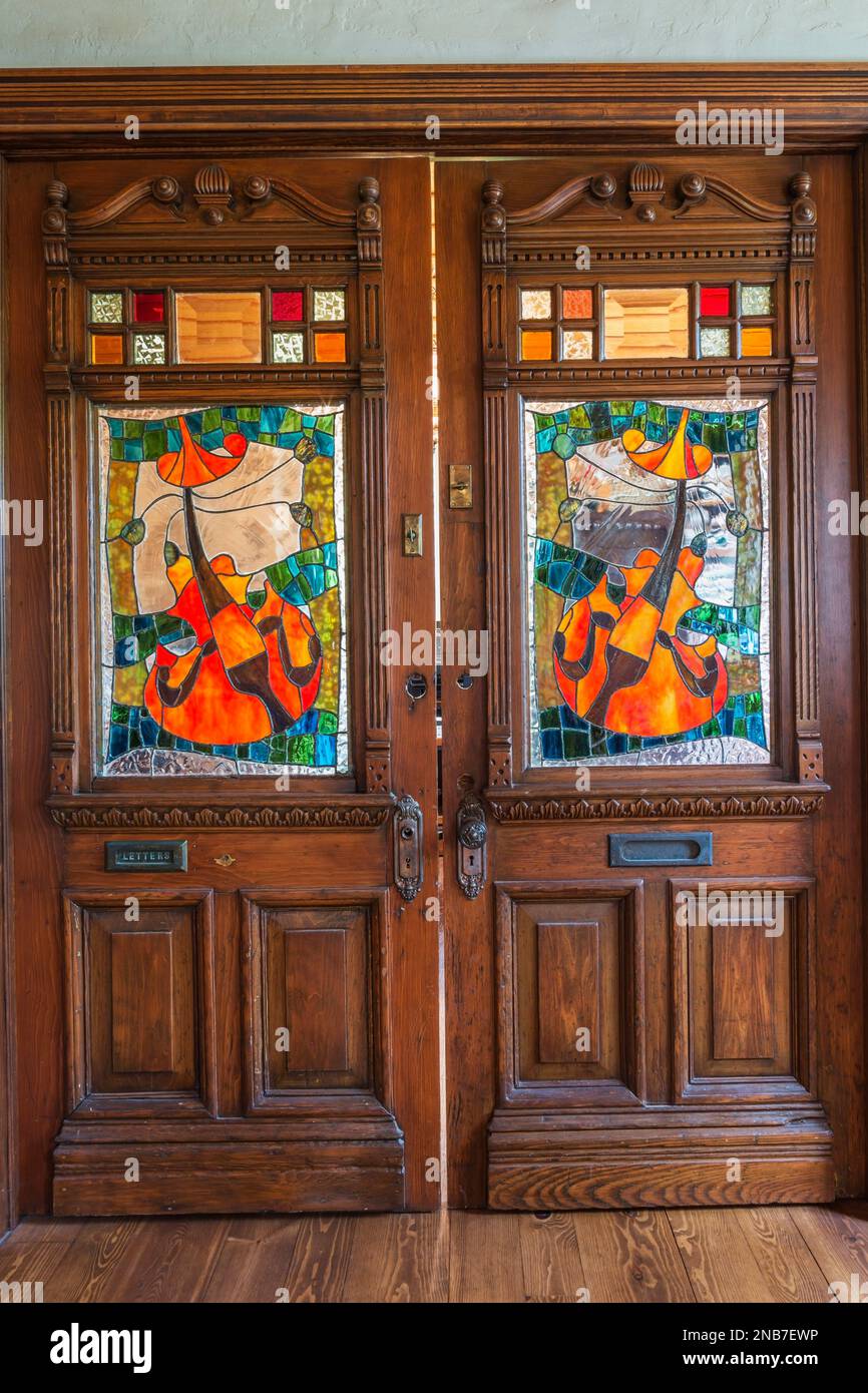 Old wooden doors with stained glass windows and carved details in living room inside old 1826 cottage style fieldstone house. Stock Photo