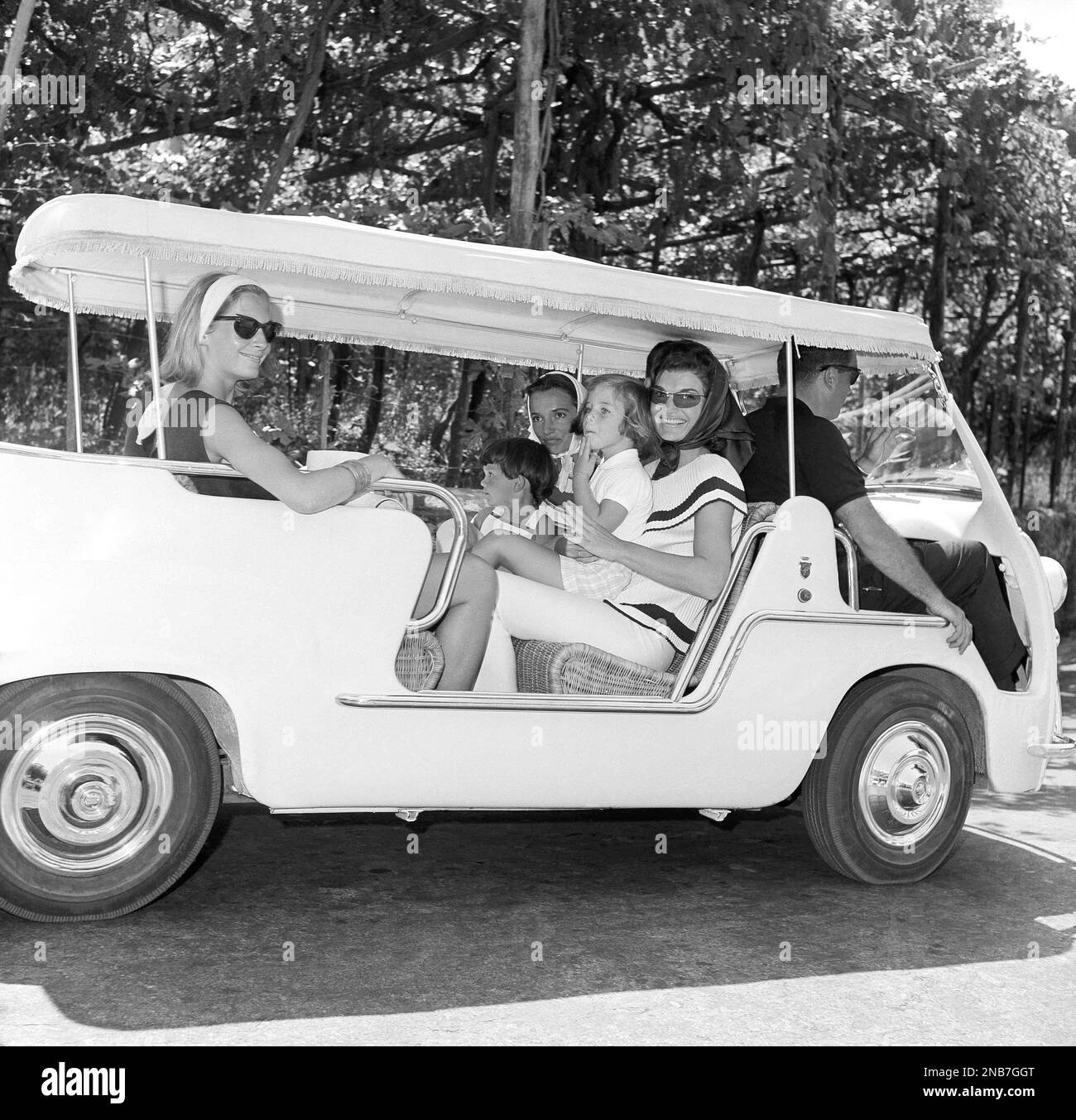 Smiling Mrs. Jacqueline Kennedy, wearing slacks and dark glasses, holds ...
