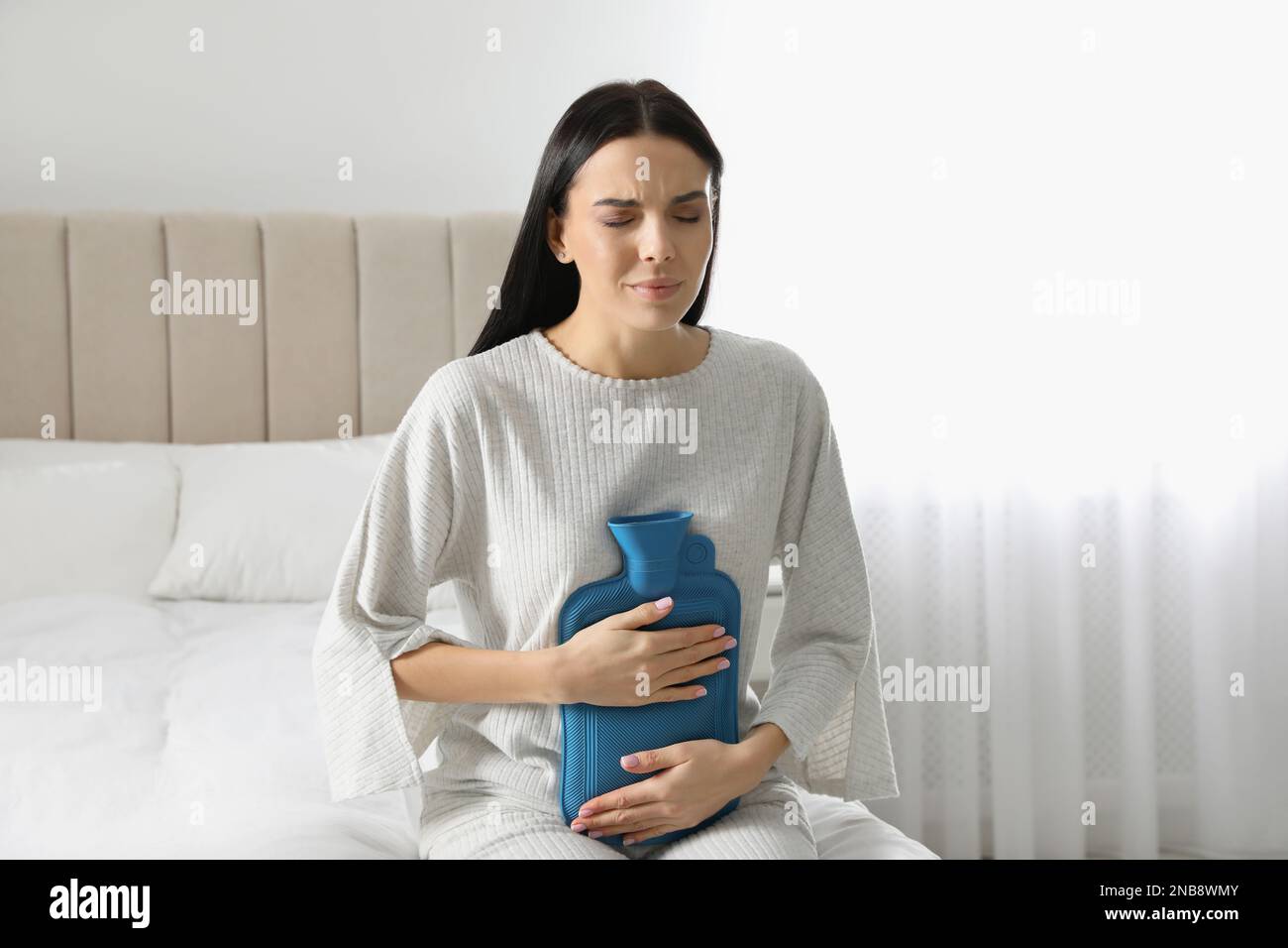Woman using hot water bottle to relieve abdominal pain on bed at home
