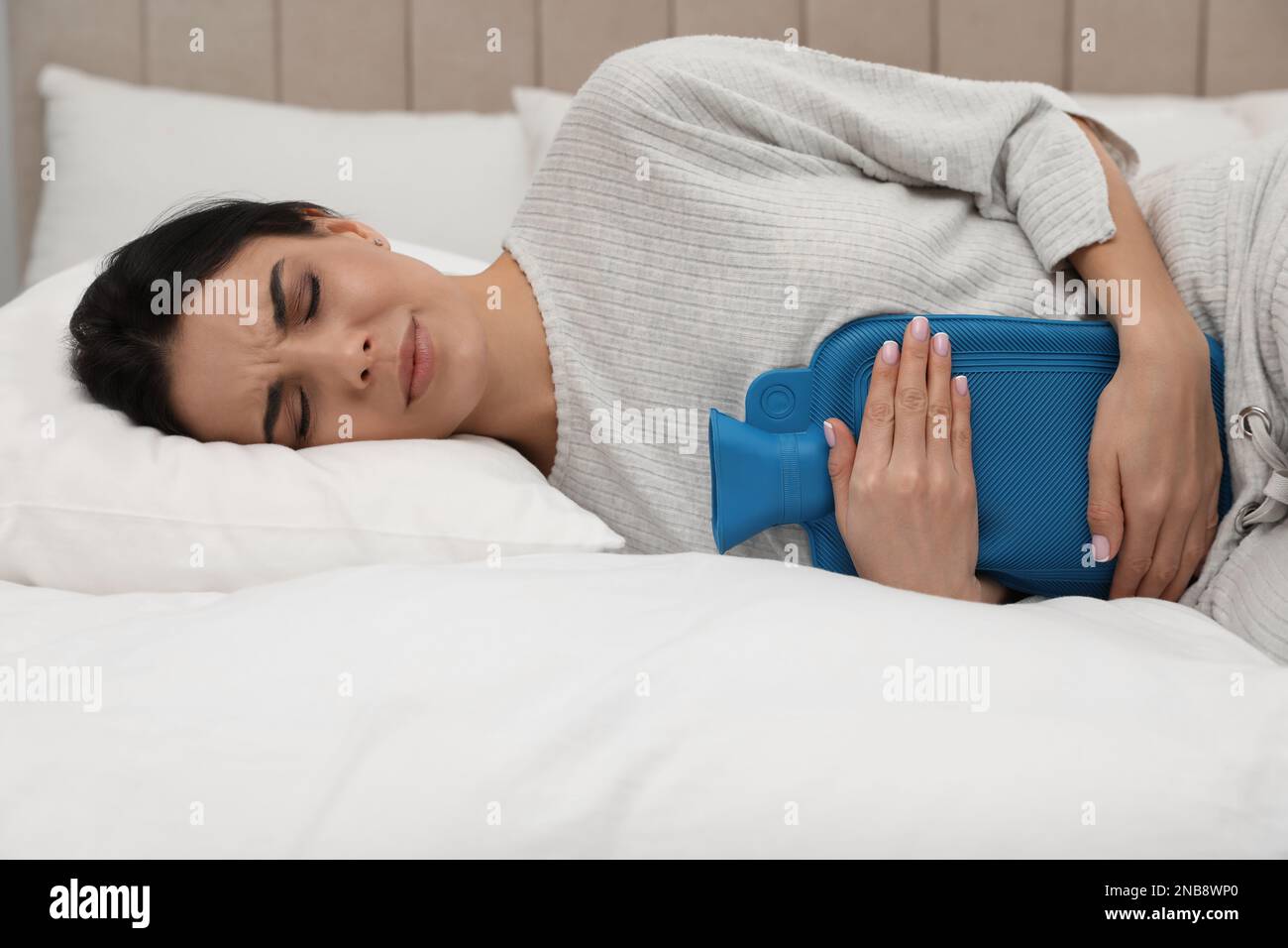 Woman using hot water bottle to relieve menstrual pain on bed at home