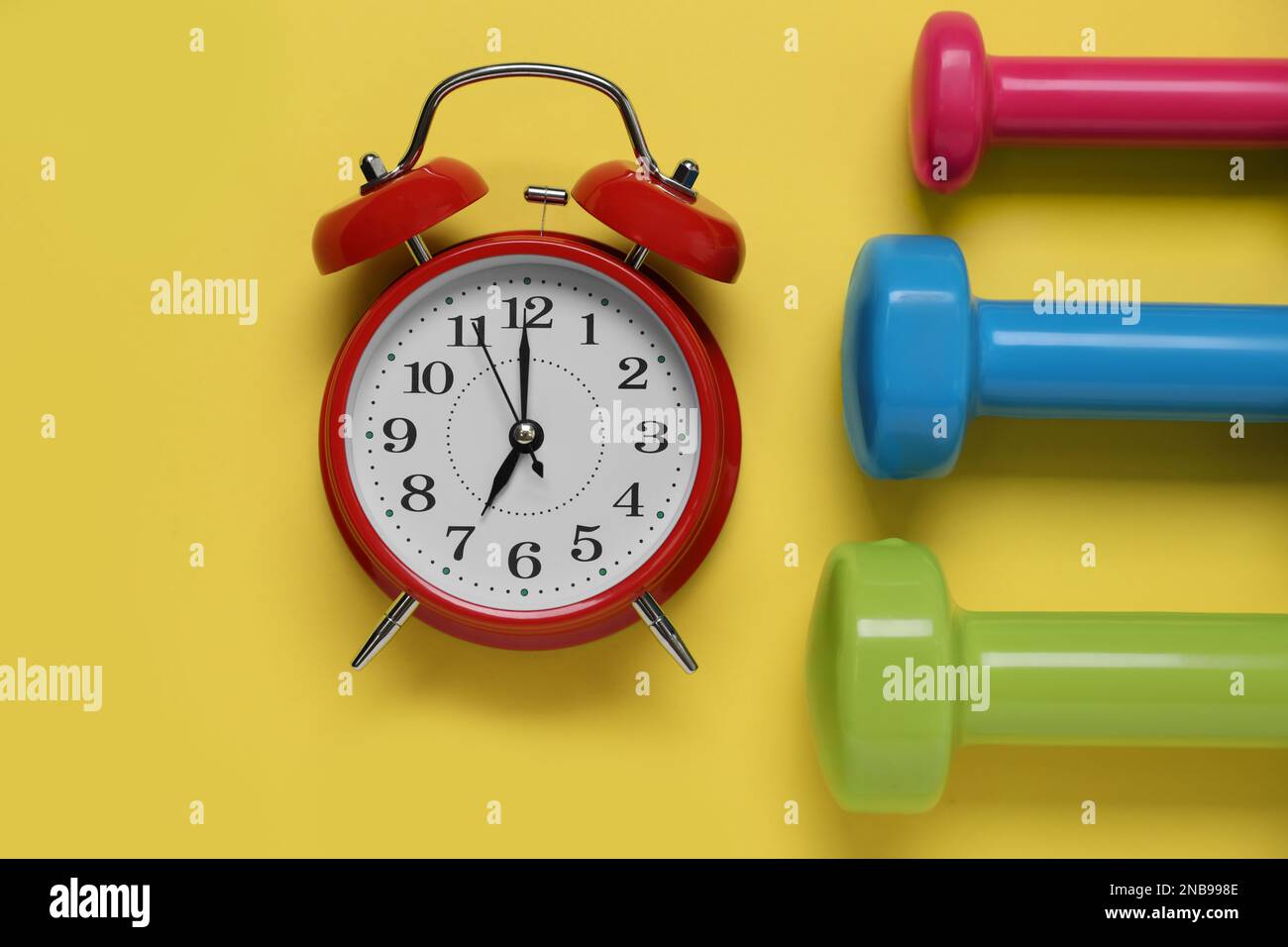 Alarm clock and dumbbells on yellow background, flat lay. Morning