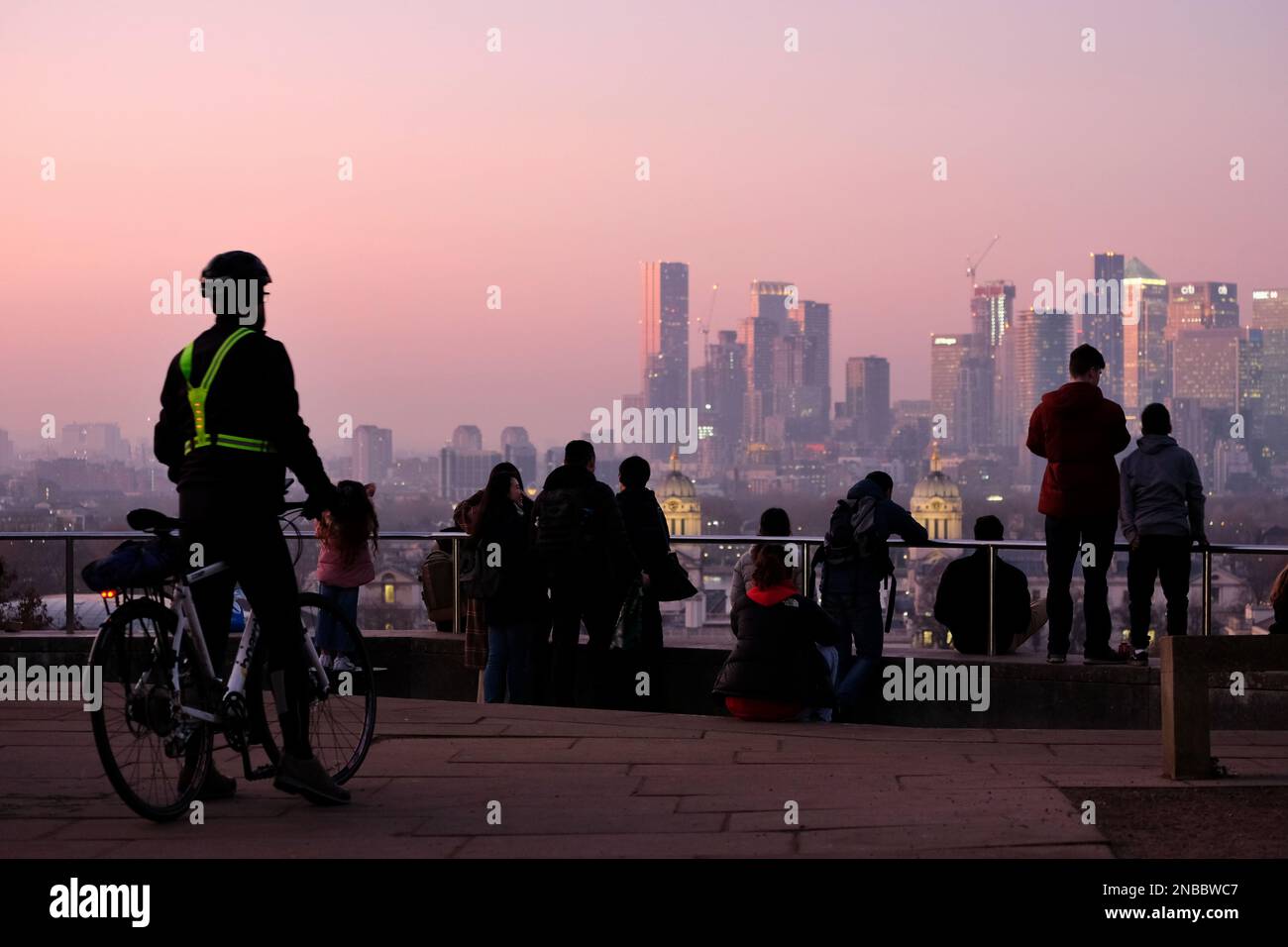 London, UK. 13th February, 2023. A cyclist looks at the view from Greenwich Park. Hazy conditions were observed at Greenwich Park during sunset and dusk, as southerly winds are expected to bring Saharan dust deposits to the UK, which will peak between Tuesday and Wednesday. The mineral dust in the atmosphere can turn skies an orange hue, cause 'blood rain' and spectacular sunrises and sunsets. Credit: Eleventh Hour Photography/Alamy Live News Stock Photo