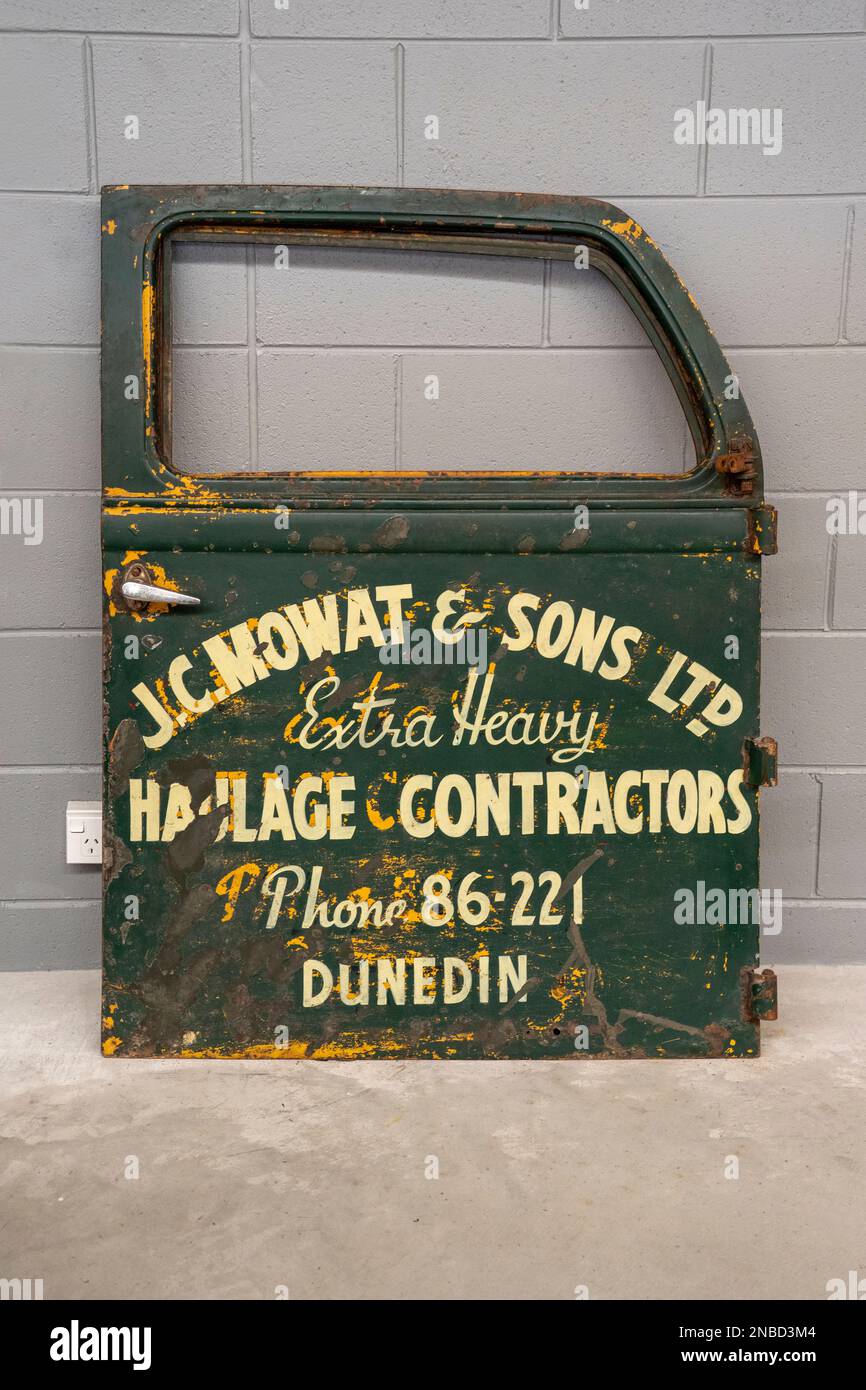 Invercargill, South Island, New Zealand- January, 2023: A dark green, rusted old truck door with a pale yellow sign J C Mowat and Sons Ltd. Extra Heav Stock Photo