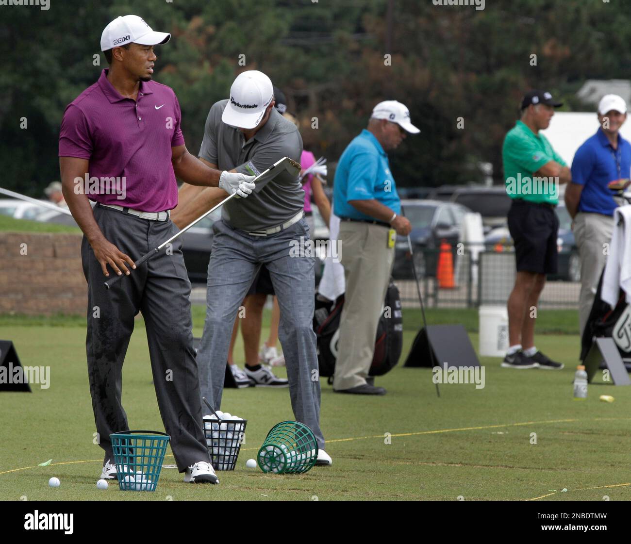 As Tiger Woods, left, watches his shot on the driving range before the