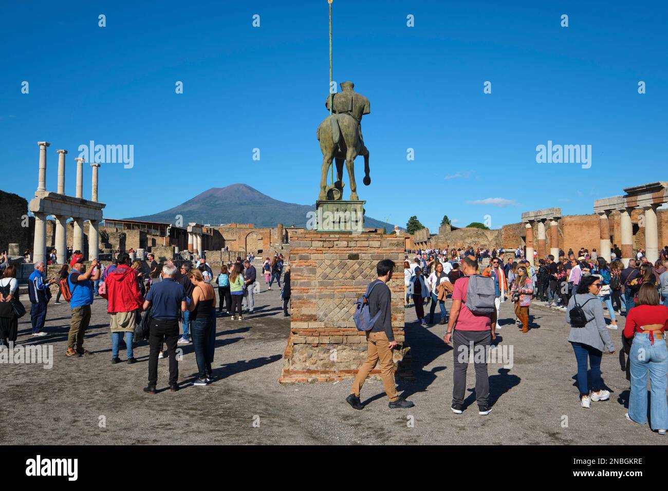 Groups of tourists, visitors pack, crowd the forum area, busy posing for photographs, selfies. At Pompeii Archaeological Park near Naples, Italy. Stock Photo