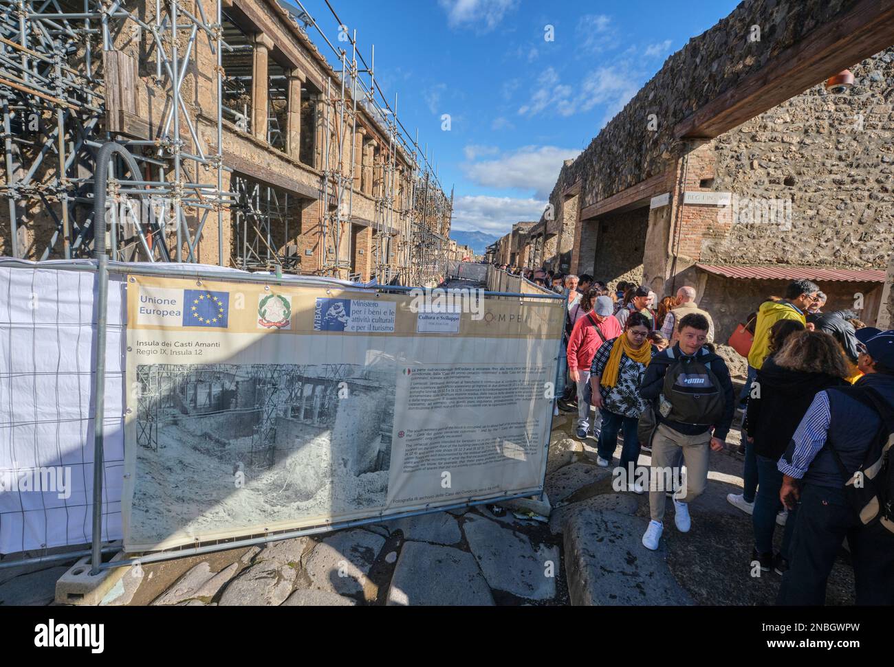 Preservation, restoration work with metal scaffolding being done at a two story villa building. Tourists are stuck traversing a small area. At Pompeii Stock Photo