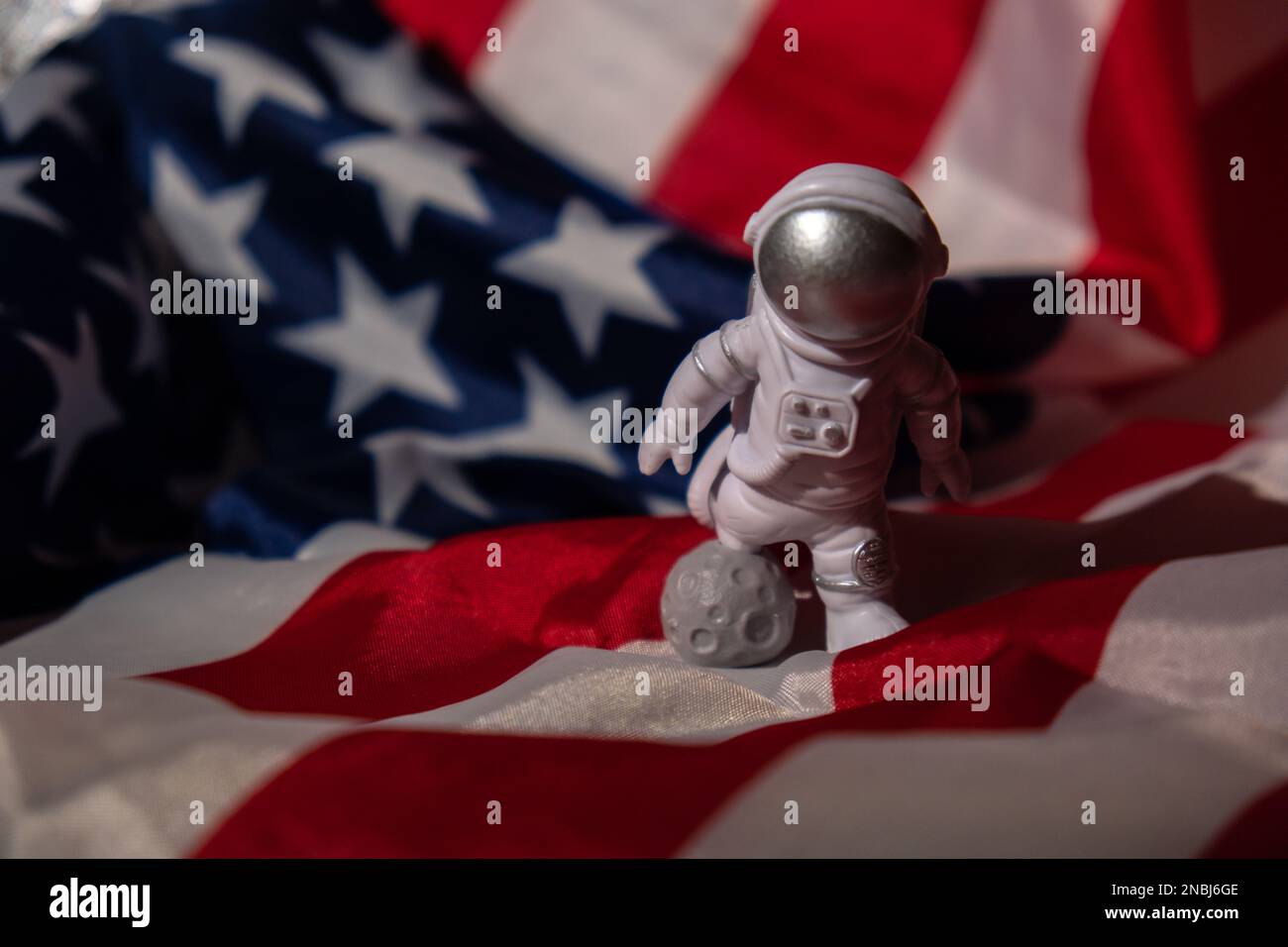 Plastic toy figure astronaut on American flag background Copy space. 50th Anniversary of USA Landing on The Moon Concept of out of earth travel, private spaceman commercial flights. Space missions and Sustainability Stock Photo