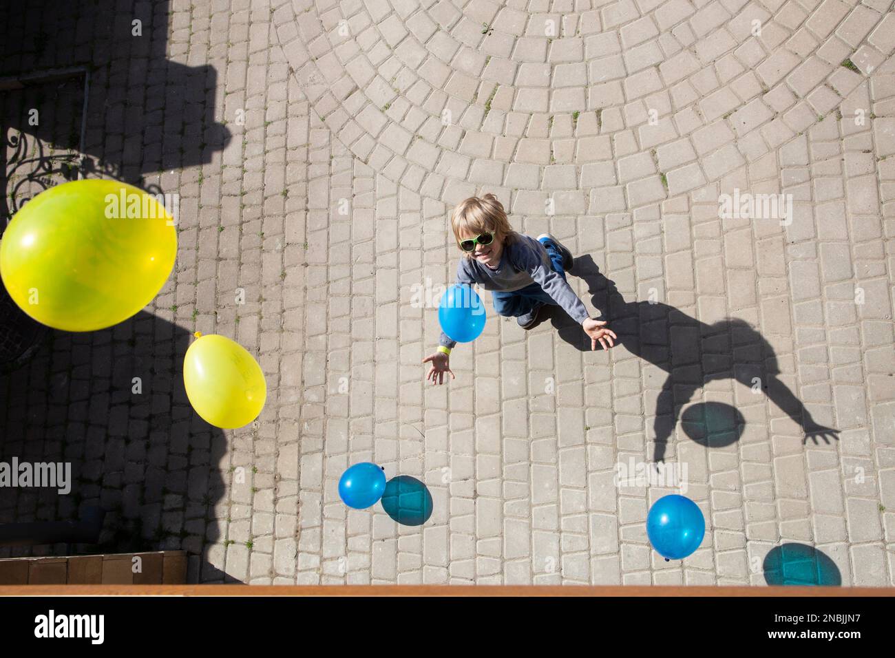 boy catches lot of yellow and blue balls falling on him from above. Ukrainian children against war. Drawing attention to war in Ukraine. happy childho Stock Photo