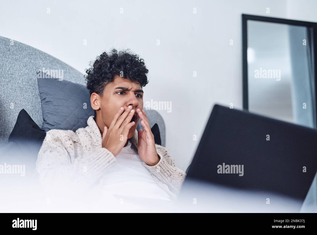 Lockdown, suddenly everyones a reality tv fan. a young man looking shocked while using a laptop on his bed at home. Stock Photo