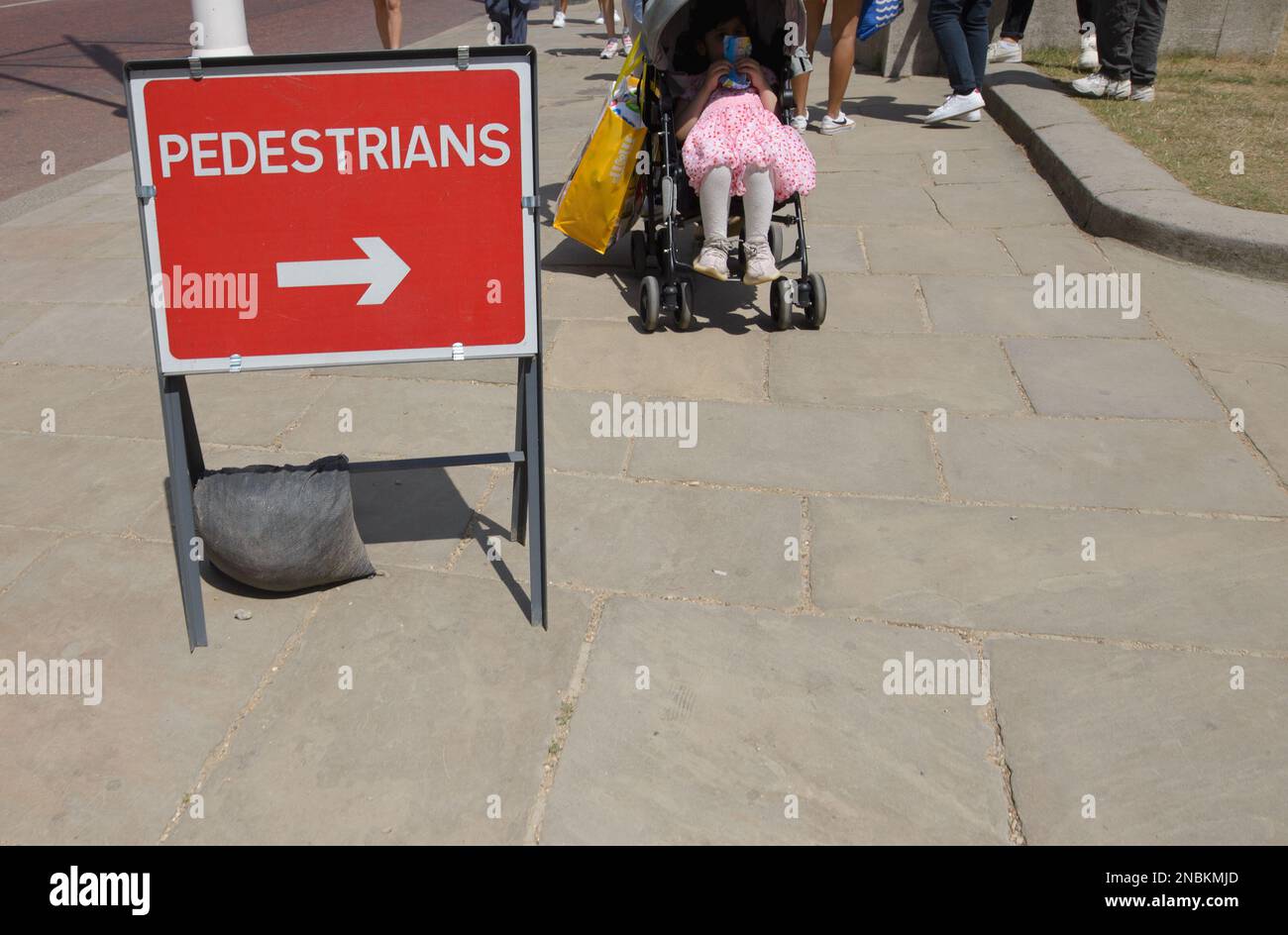 London, England, UK. Young girl in a pushchair passing a Pedestrians sign by roadworks closing off the pavement ahead Stock Photo