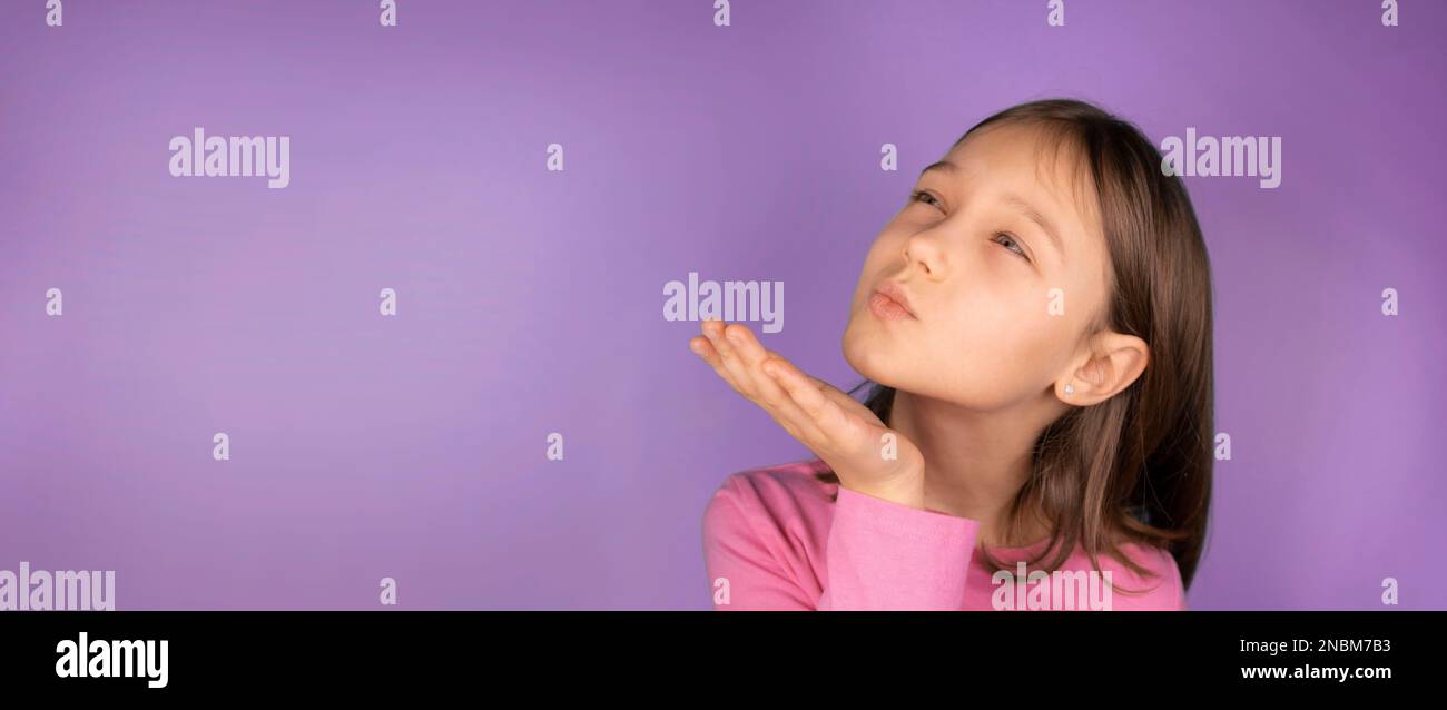 girl 8 years old sends an air kiss on a pink or purple background with a place to insert. copy space Stock Photo