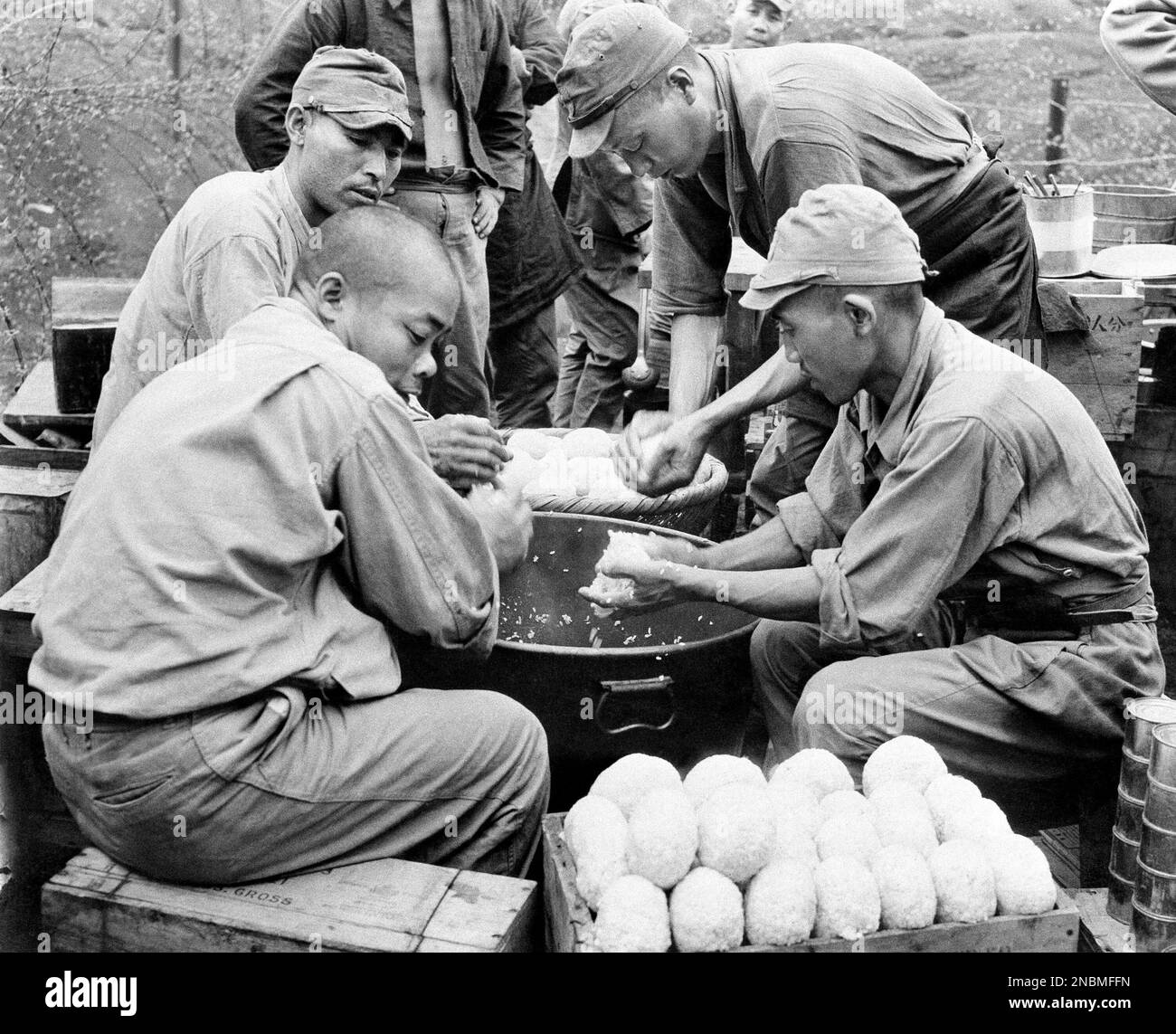 Japanese prisoners sit on packing cases around a huge kettle of rice as