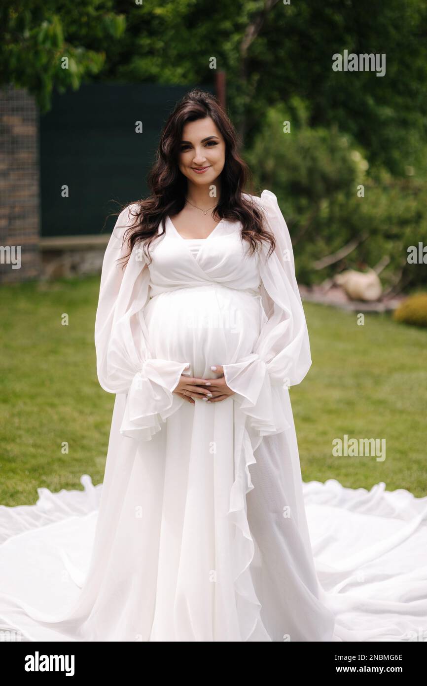 Elegant pregnant woman in beautiful white dress walking outdoors Stock ...