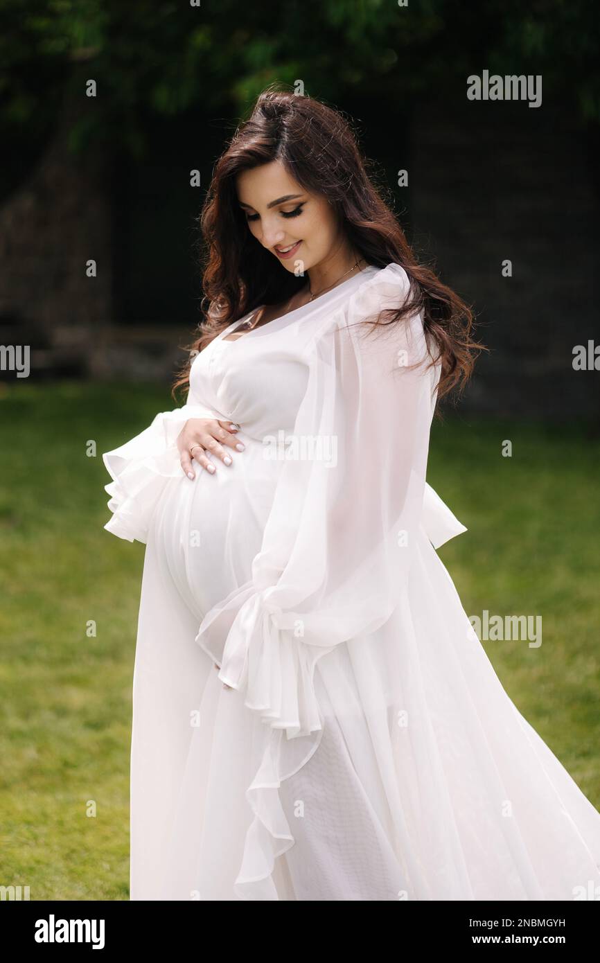 Elegant pregnant woman in beautiful white dress walking outdoors Stock ...