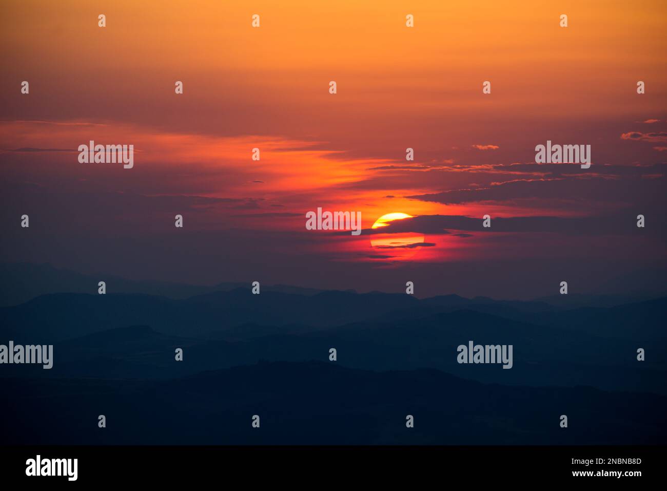 A red sun setting behind mountain and making clouds red Stock Photo - Alamy