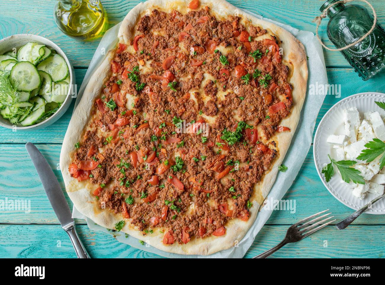 Turkish pizza or lahmacun with ground beef, vegetables. Served with feta cheese and cucumber salad on turquoise background. Flat lay Stock Photo