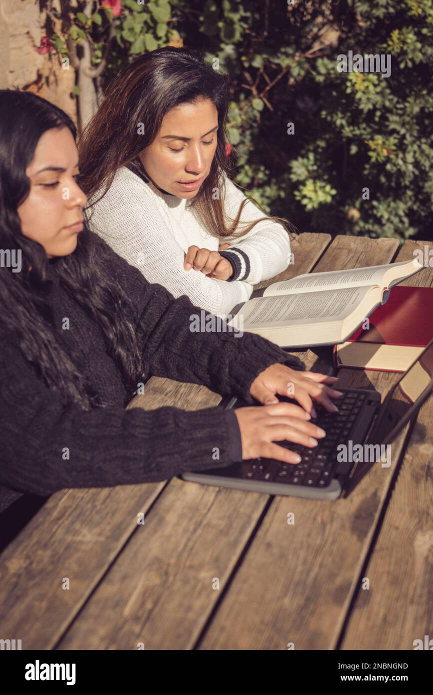young mother helps daughter do college work, in home garden Stock Photo
