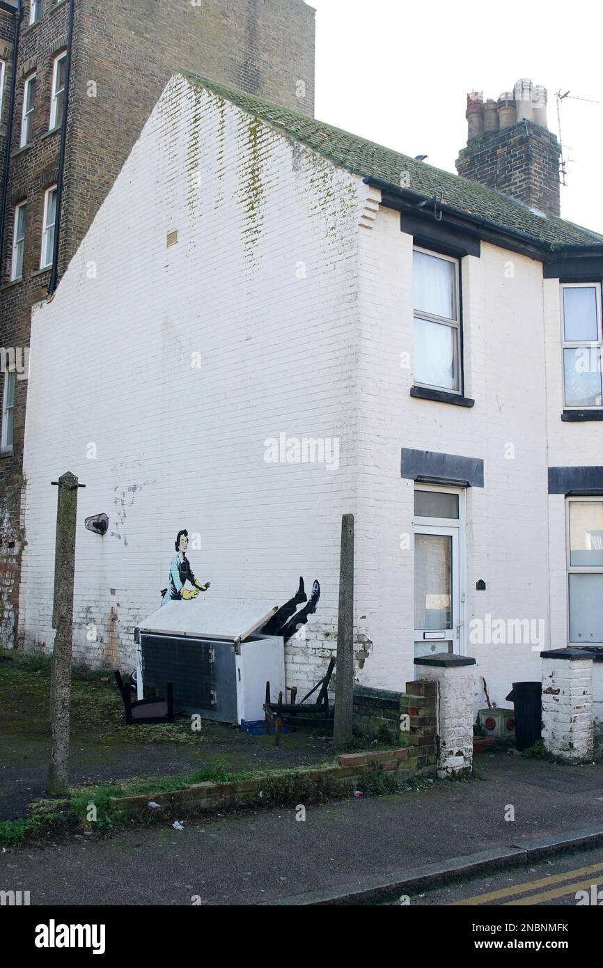 A new artwork by street artist Banksy, titled 'Valentine's Day Mascara' on the side of a building in Margate, Kent. The artwork depicts a 1950's housewife, wearing a classic blue pinny and yellow washing up gloves, with a swollen eye and a missing tooth seemingly shoving her male partner into a chest freezer. Picture date: Tuesday February 14, 2023. Stock Photo