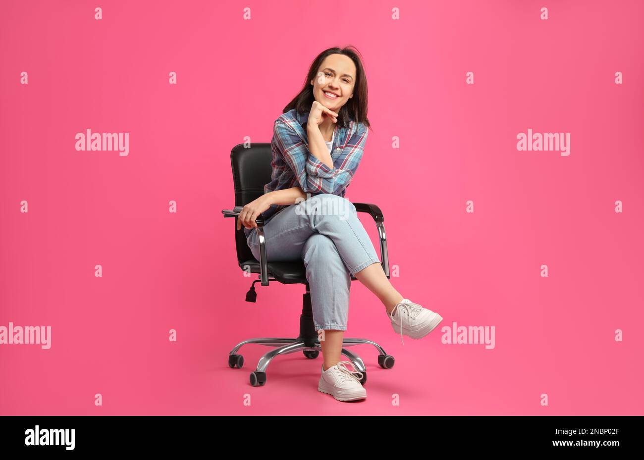 Mature woman sitting in comfortable office chair on pink background Stock Photo