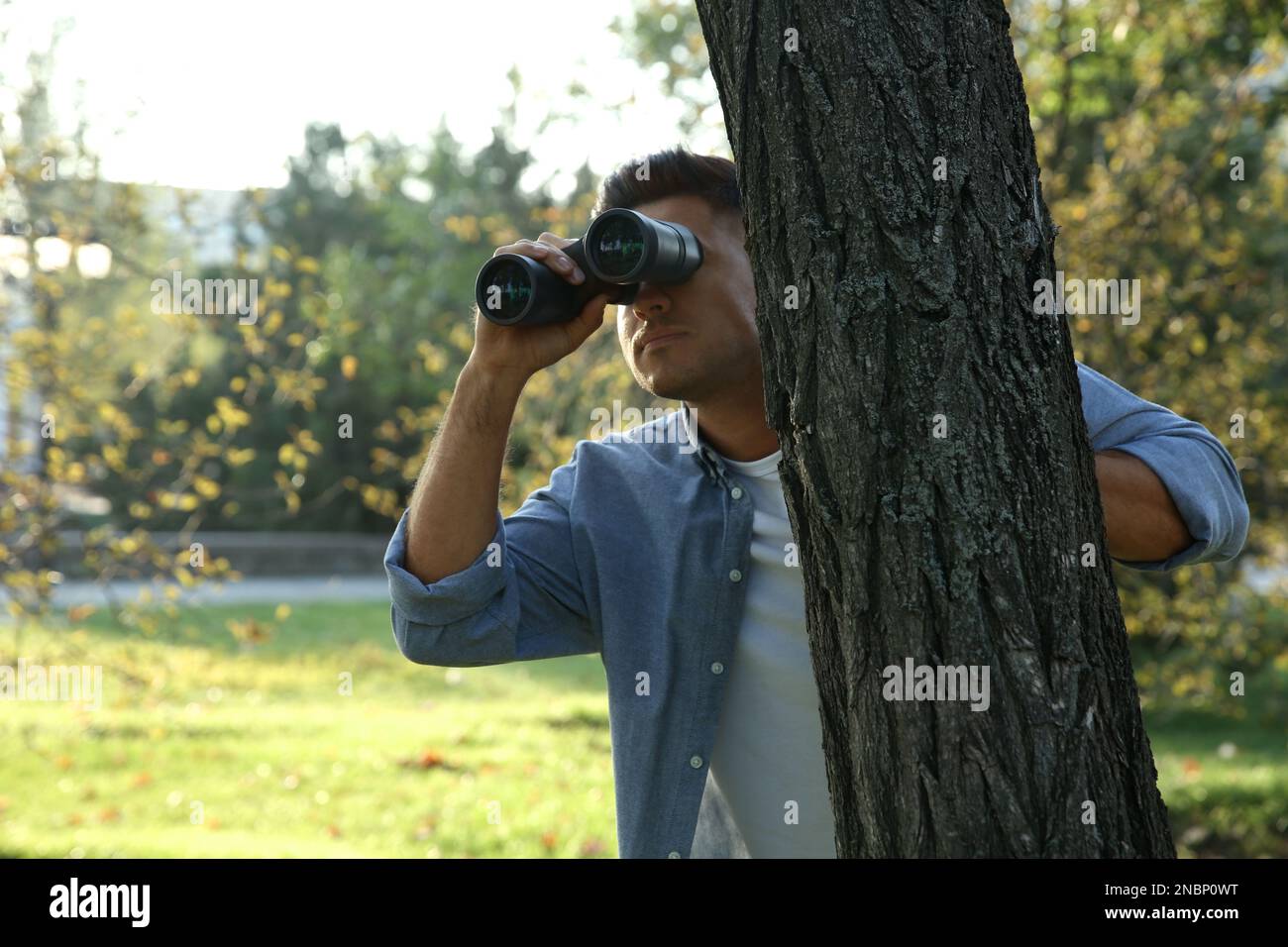 Jealous man with binoculars spying on ex girlfriend in park Stock Photo
