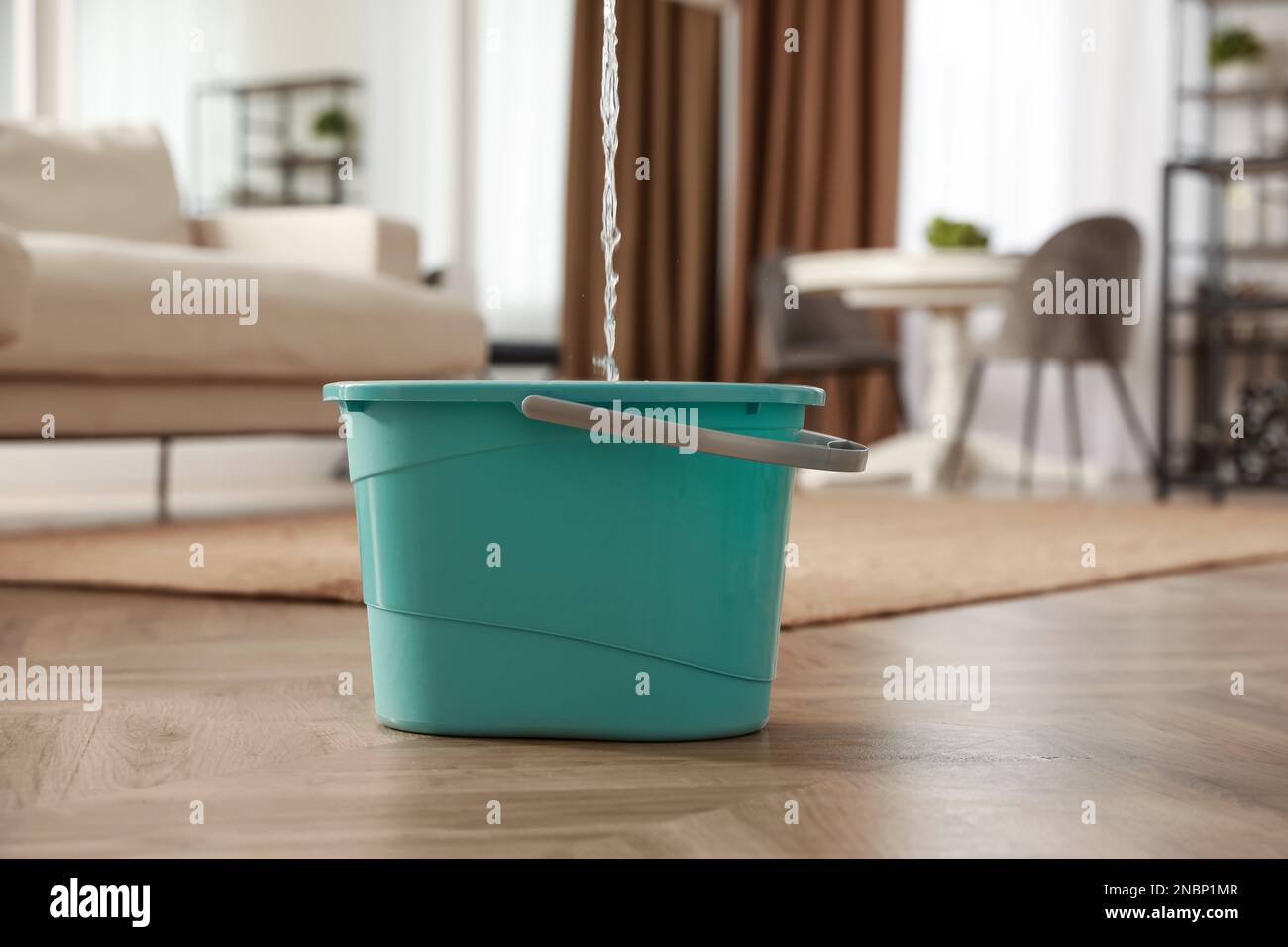 Bucket collecting water from ceiling in living room. Leaking roof Stock Photo