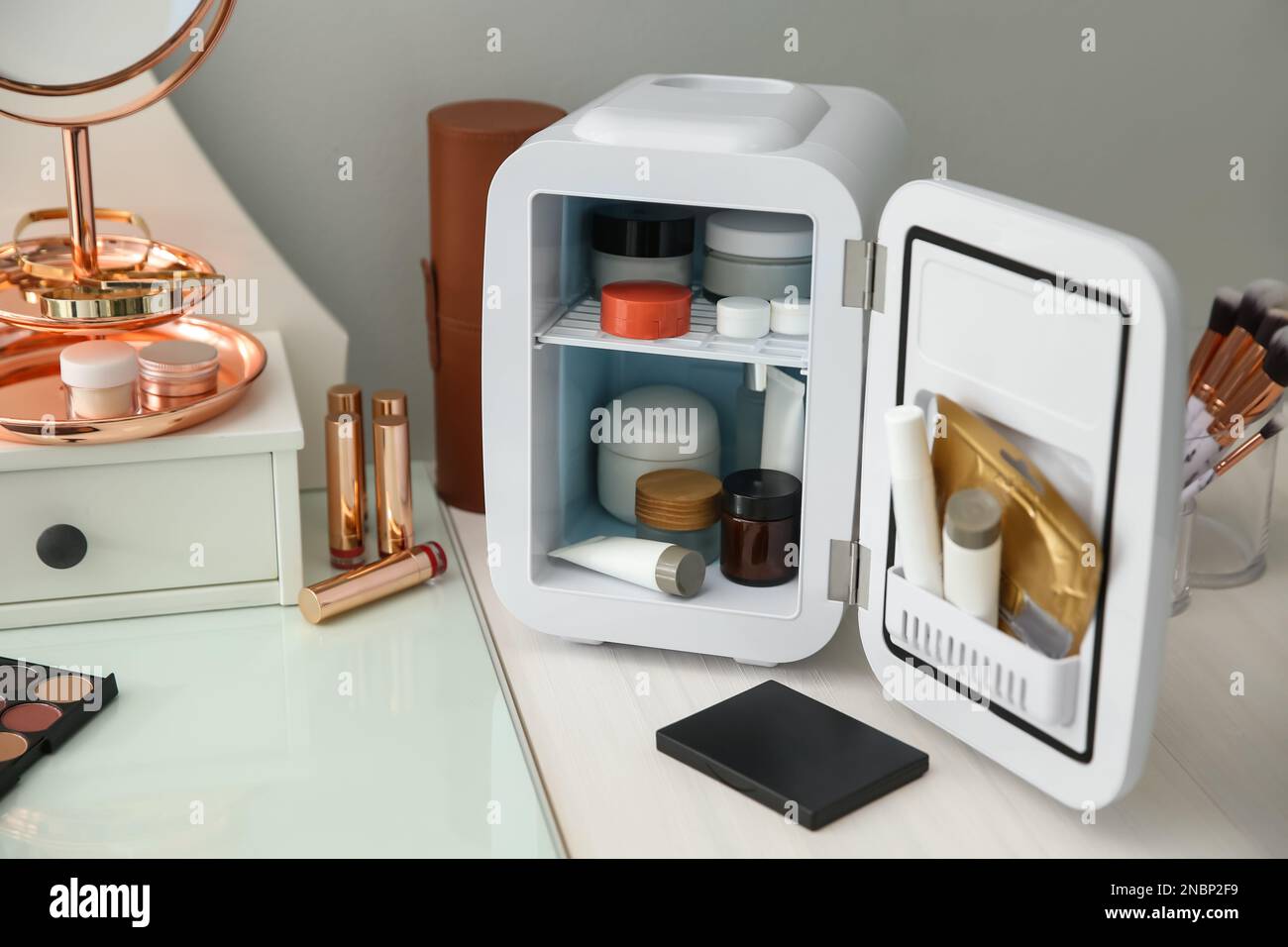 Cosmetics refrigerator and skin care products on white vanity table