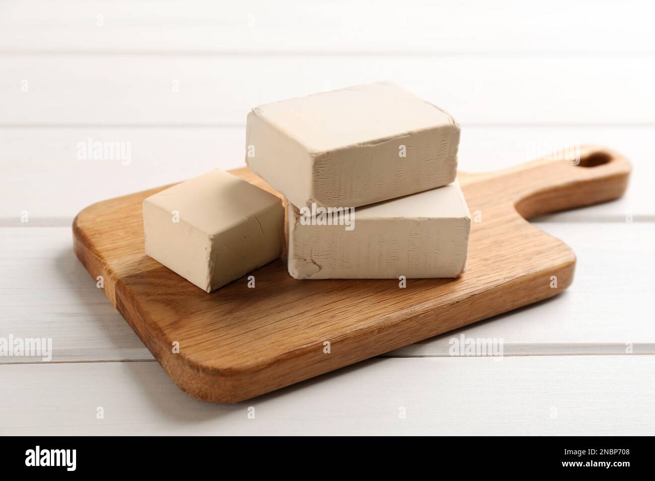 Blocks of compressed yeast with cutting board on white wooden table