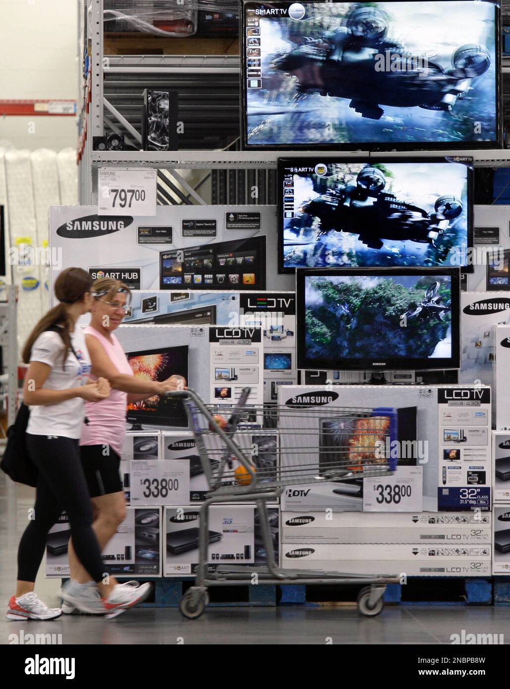 Shoppers push a cart past a television display in the electronics ...