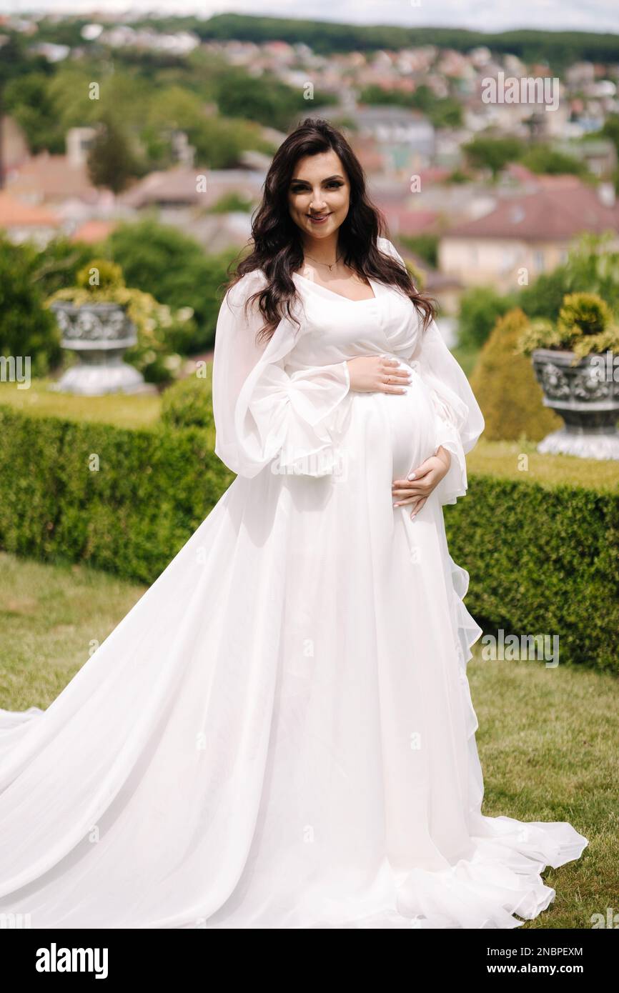 Portrait of elegant pregnant woman in beautiful white dress walking ...