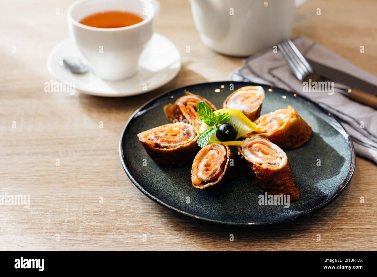 Rolls of thin pancakes with smoked salmon and cream cheese on dark plate on wooden table. Delicious and healthy breakfast or brunch Stock Photo