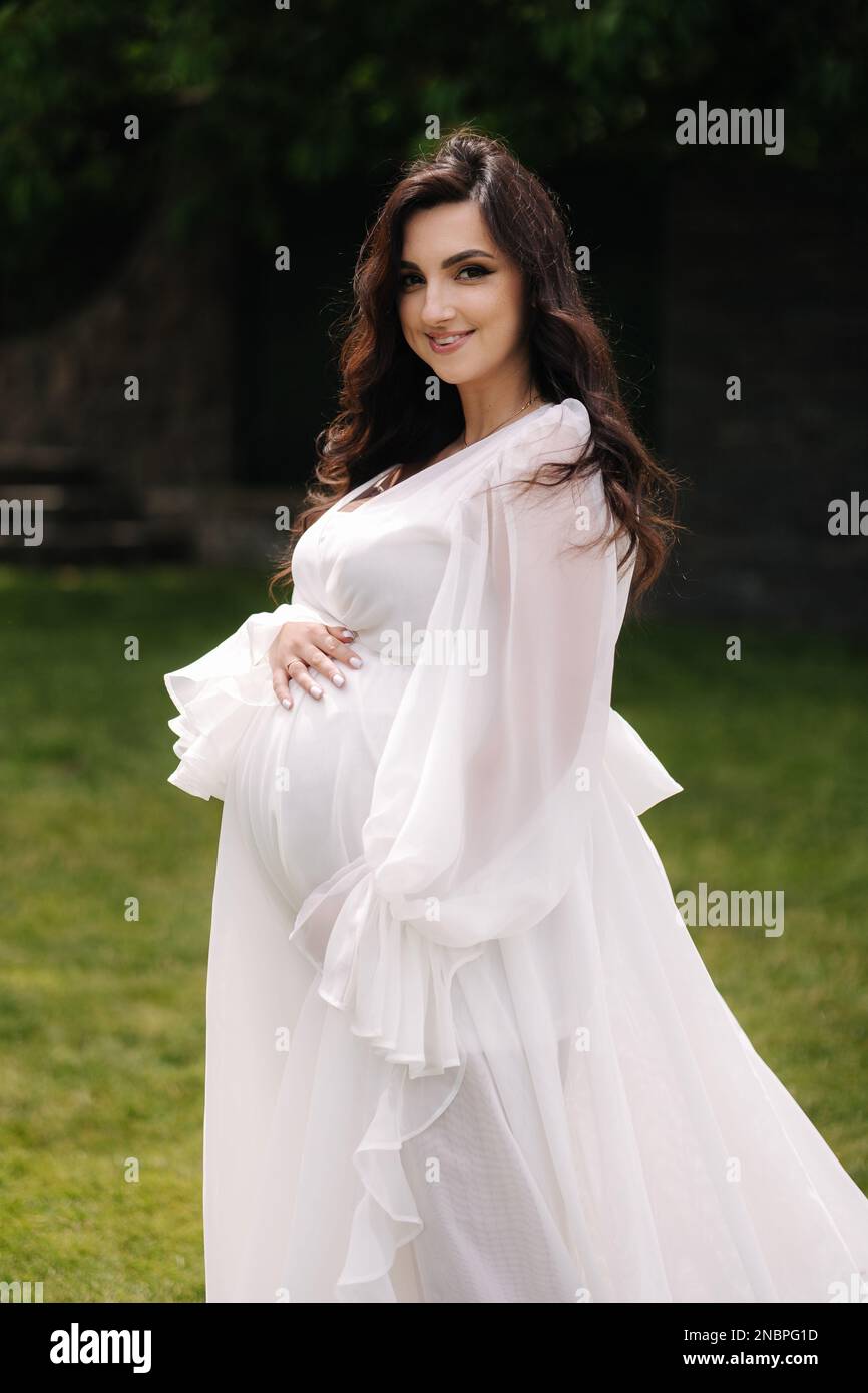 Portrait of elegant pregnant woman in beautiful white dress walking ...