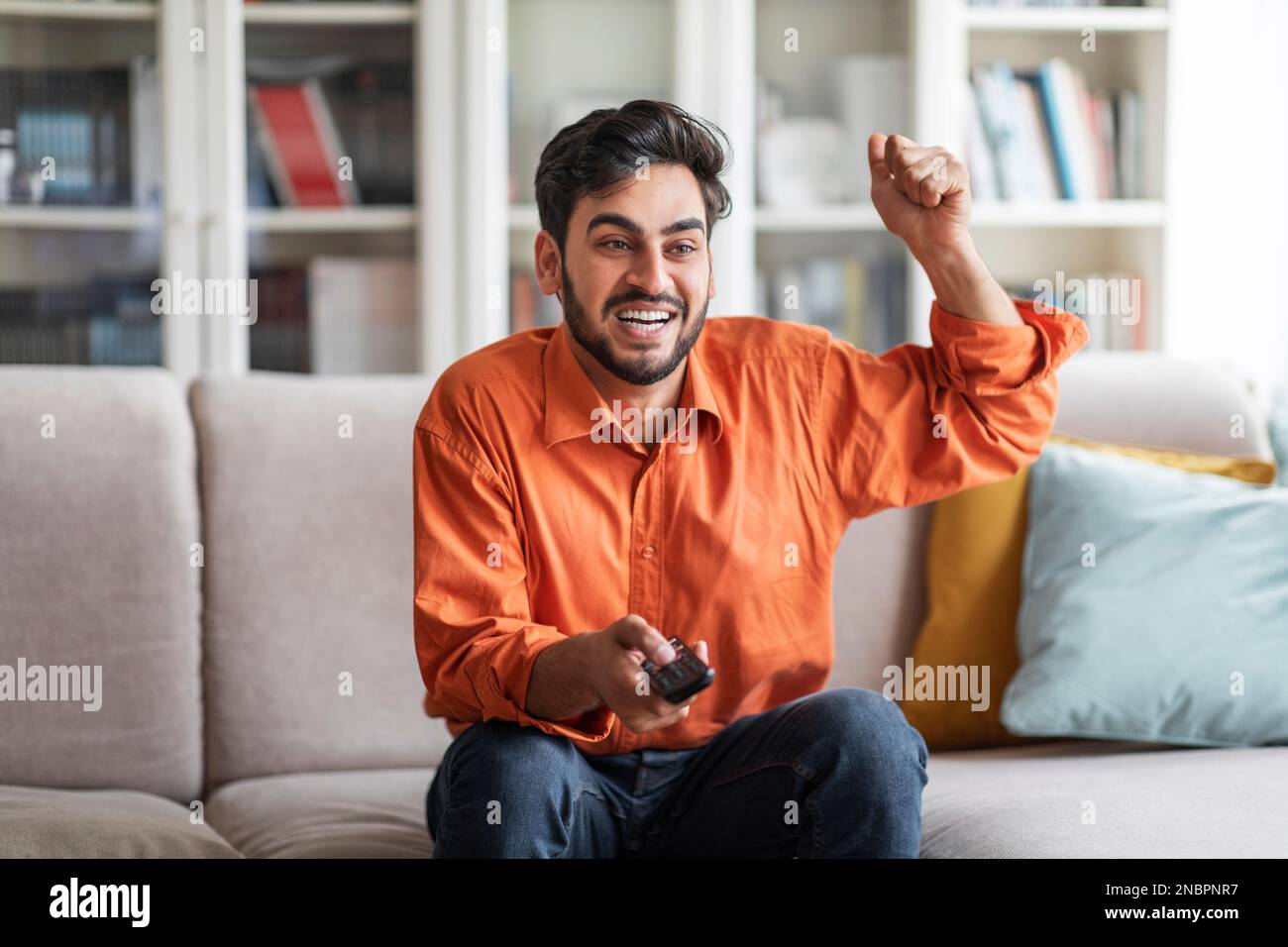 Emotional arab man watching TV at home, gesturing Stock Photo