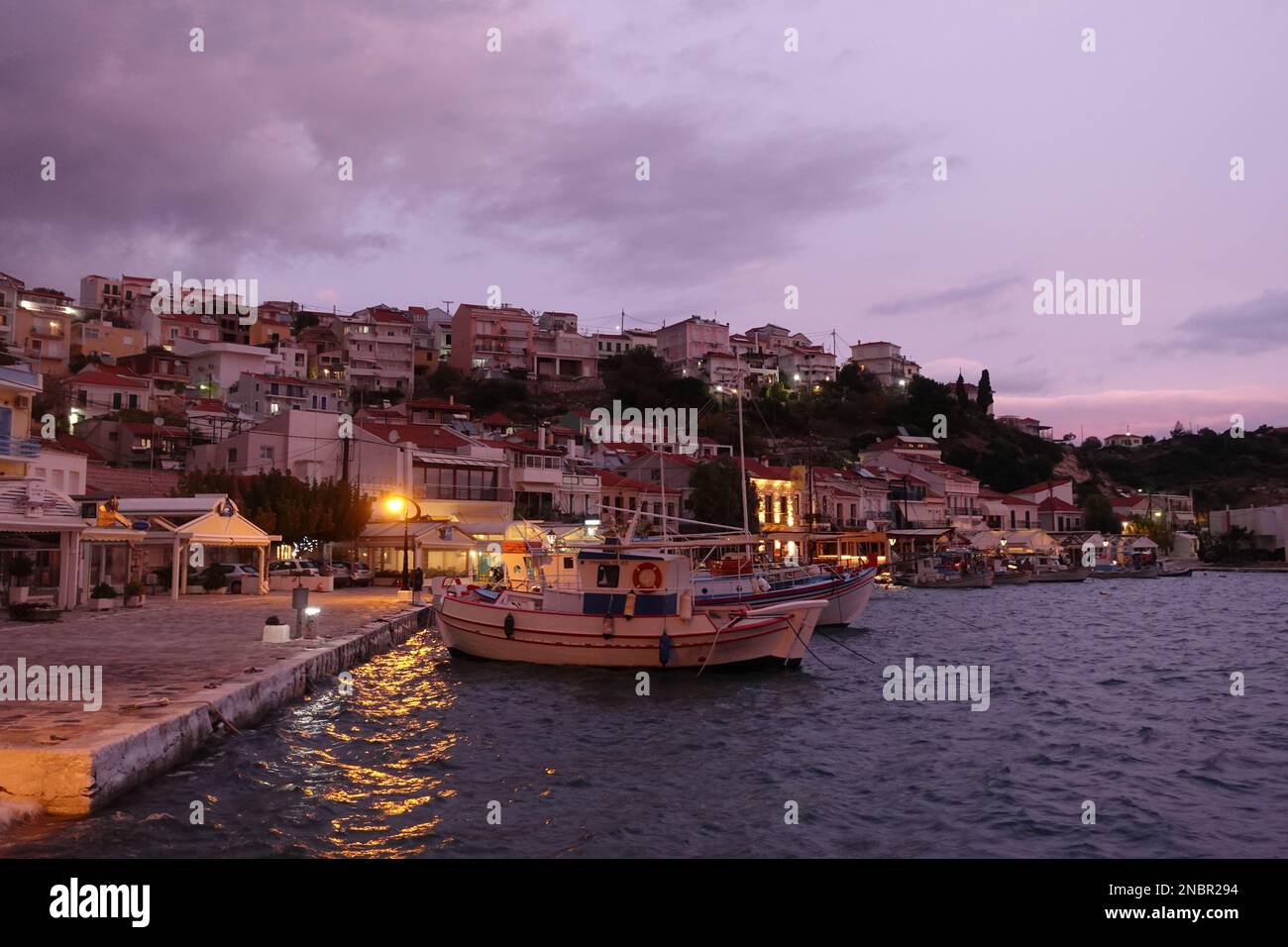 Dusk shot of the fishing boats in Pythagoreio port with the village in the background on Samos Dusk shot of the fishing boats in Pythagoreio port with the village in the background on Samos