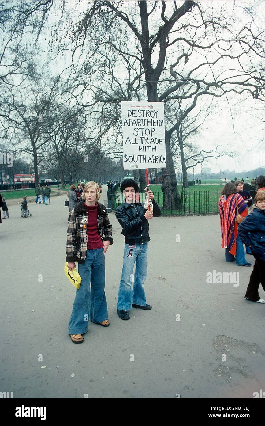 London 1977. A young man holding a handwritten sign with the text Destroy Apartheid! Stop all trade with South Africa. The two men are wearing the typical wide-legged jeans that was a 1970s fashion.   Kristoffersson ref DV2 Stock Photo