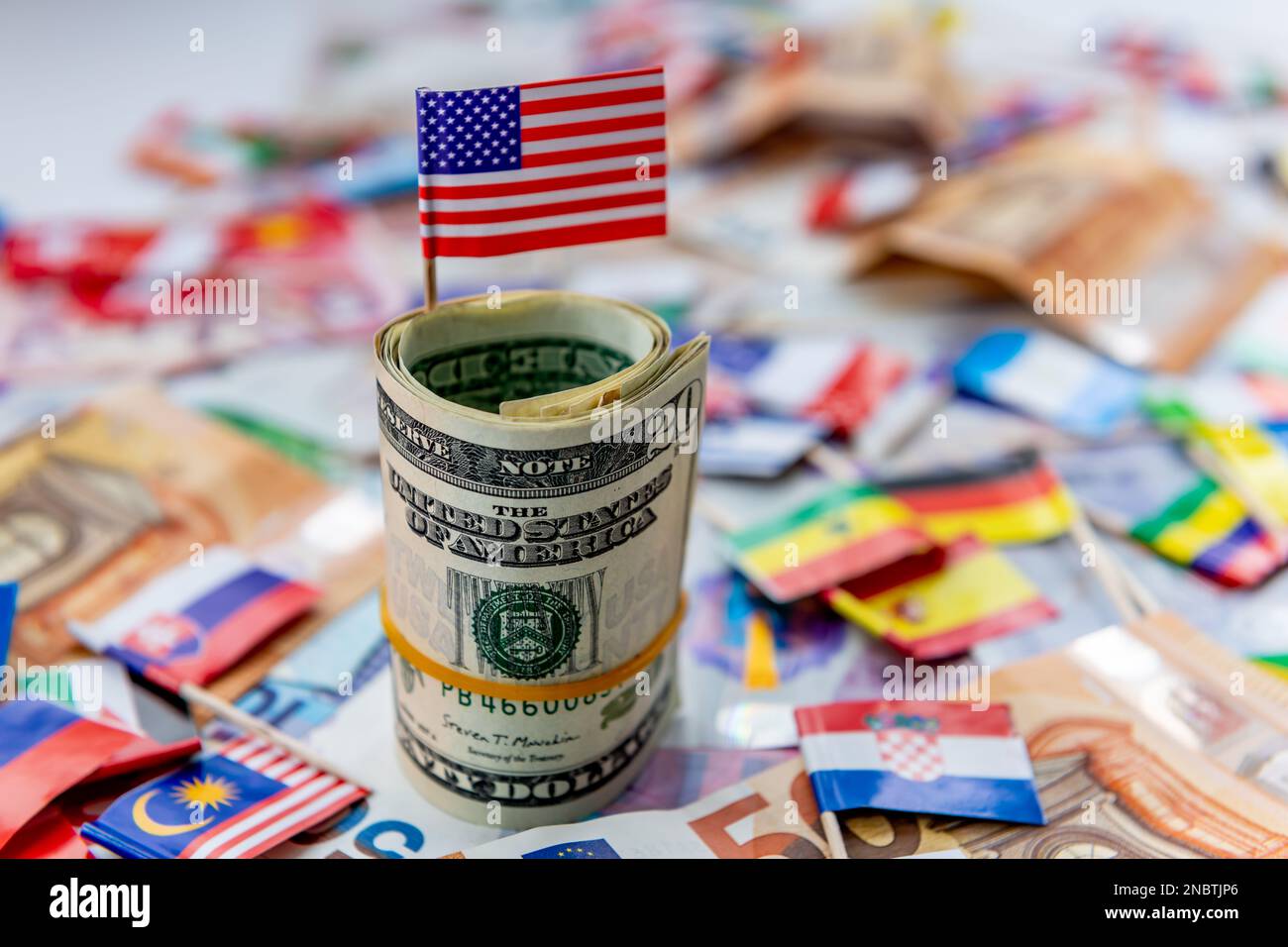 A roll of US dollars with the American flag on top of a other currencies and country flags. Dollar hegemony concept. Stock Photo