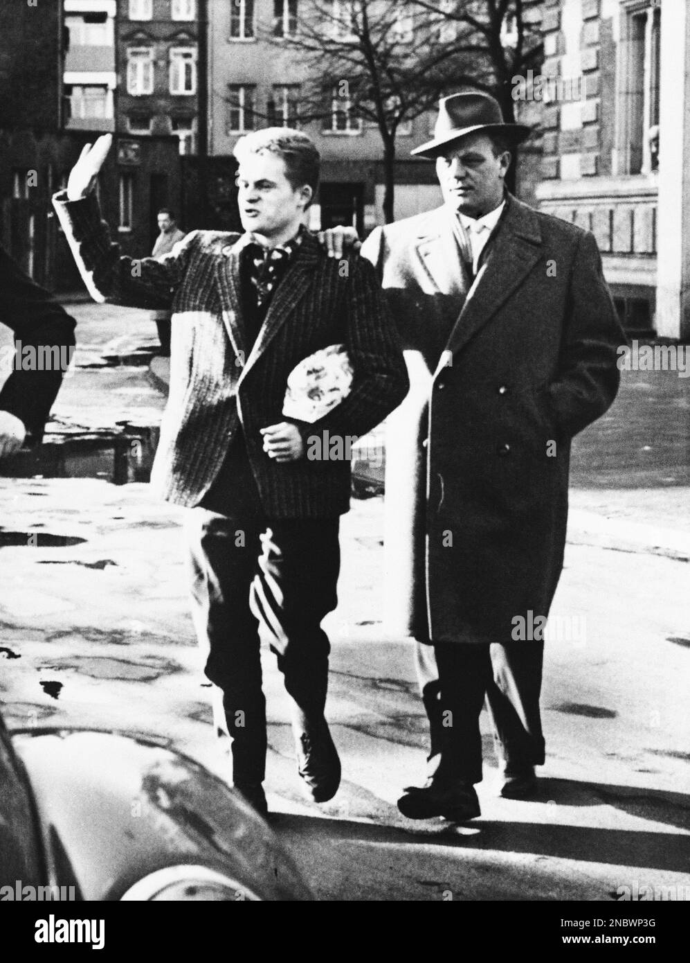 Paul Josef Schoenen, 25, held as a suspect in desecration of the Cologne,  Germany, synagogue on Christmas Eve, gives Hitler salute as he leaves  court, Dec. 26, 1959. German detective clutches Schoenen's