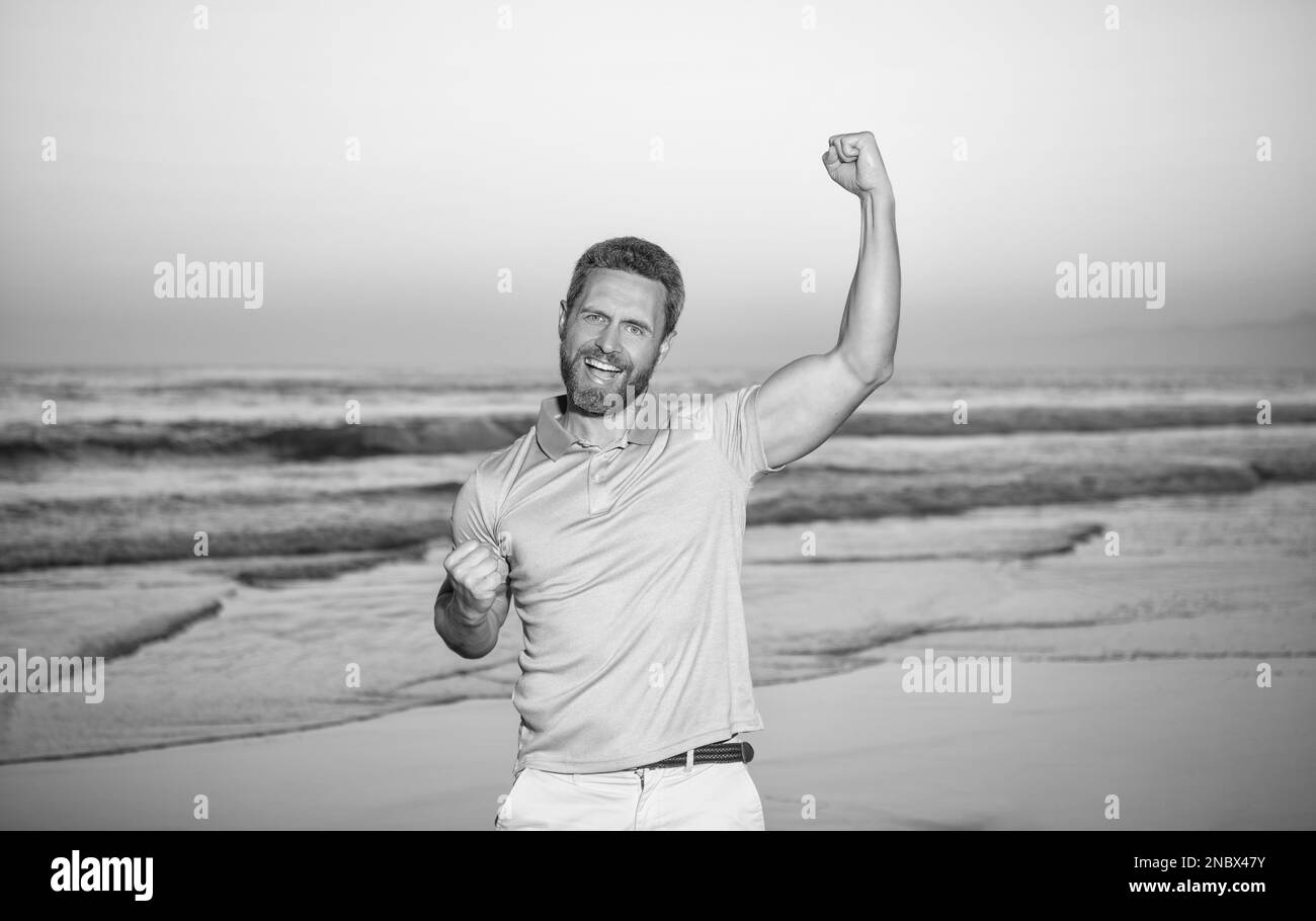 successful guy on sunrise beach. bearded man in shirt. celebrate