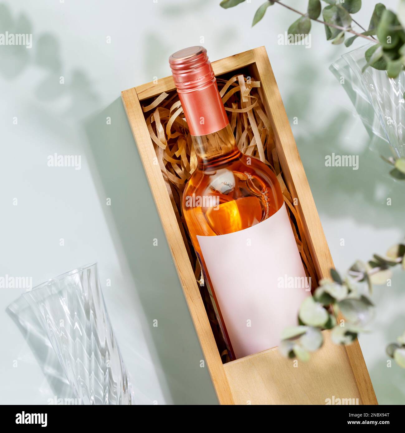 Rose wine. Bottle of pink wine with glasses on blue background with eucalyptus green leaves and shadows. Summer romantic still life with bottle of low Stock Photo