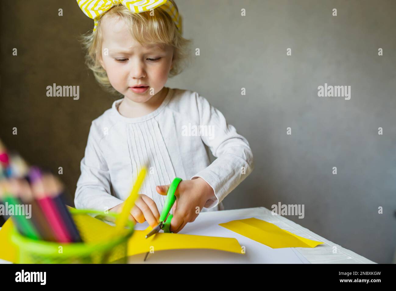 Child cutting colored paper with scissors at table in classroom. School project for children