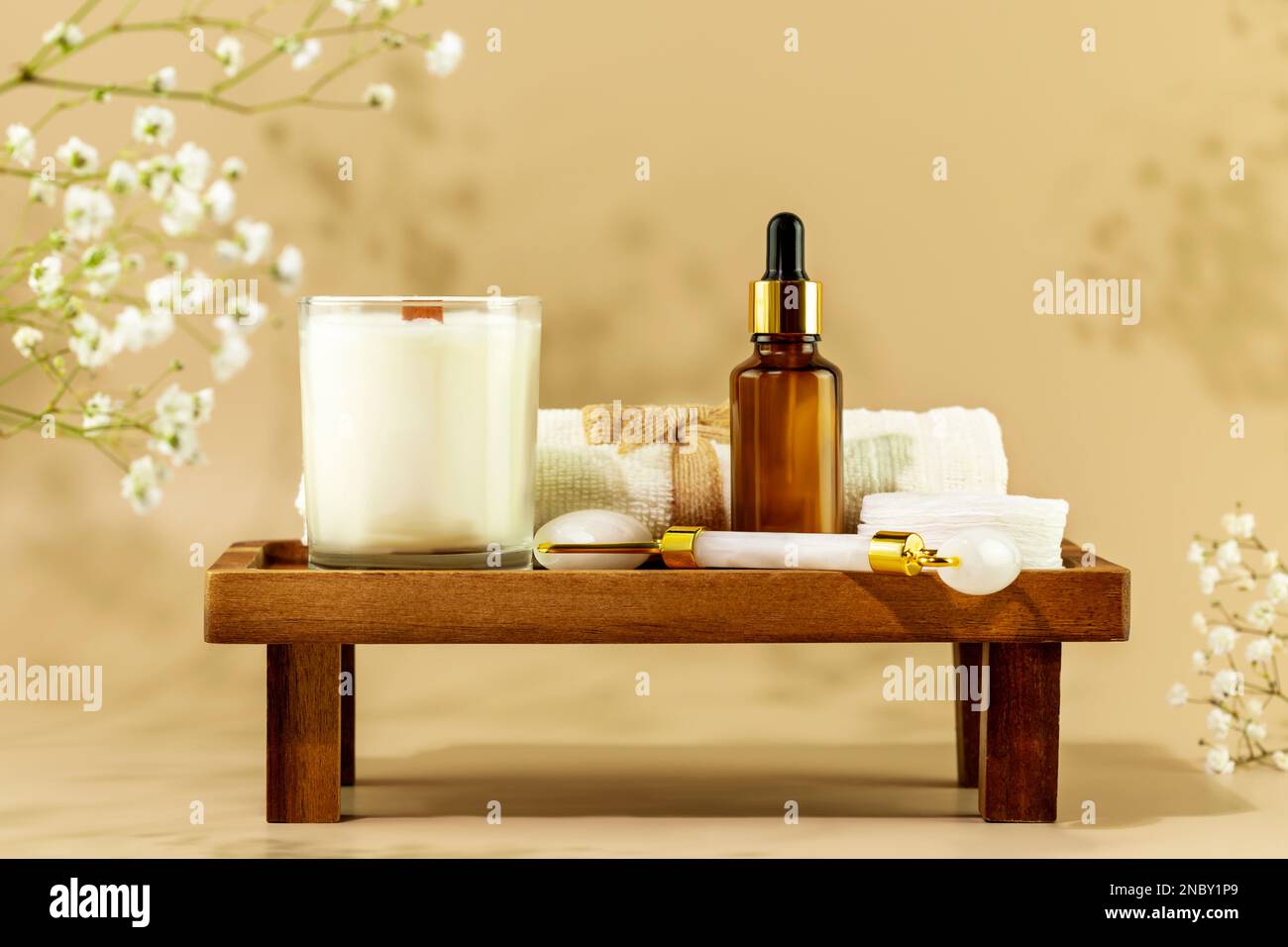Eco friendly spa relax composition with serum, face roller, towel and candle on wooden podium on beige background with white flowers. Wellness and ski Stock Photo