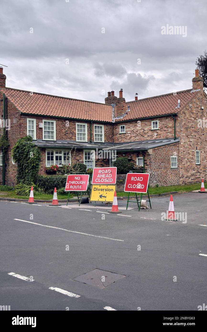 A cluster of roadworks signs - road closed, diversion, no through route - and traffic cones block a suburban street while repairs are carried out. Stock Photo