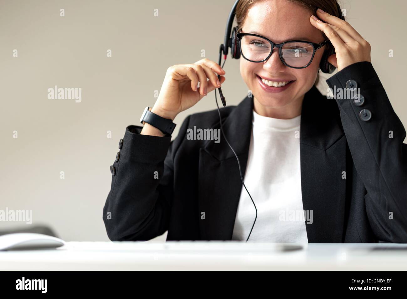 Young woman businesswoman in headset participating in business online meeting and smiling. Stock Photo