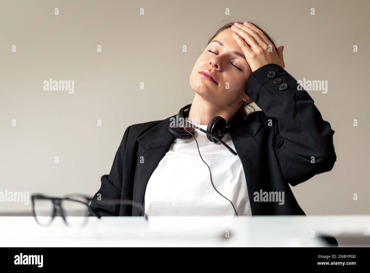 Woman office worker sitting at desk has headache touching forehead with her hand, feeling unwell at work. Stock Photo