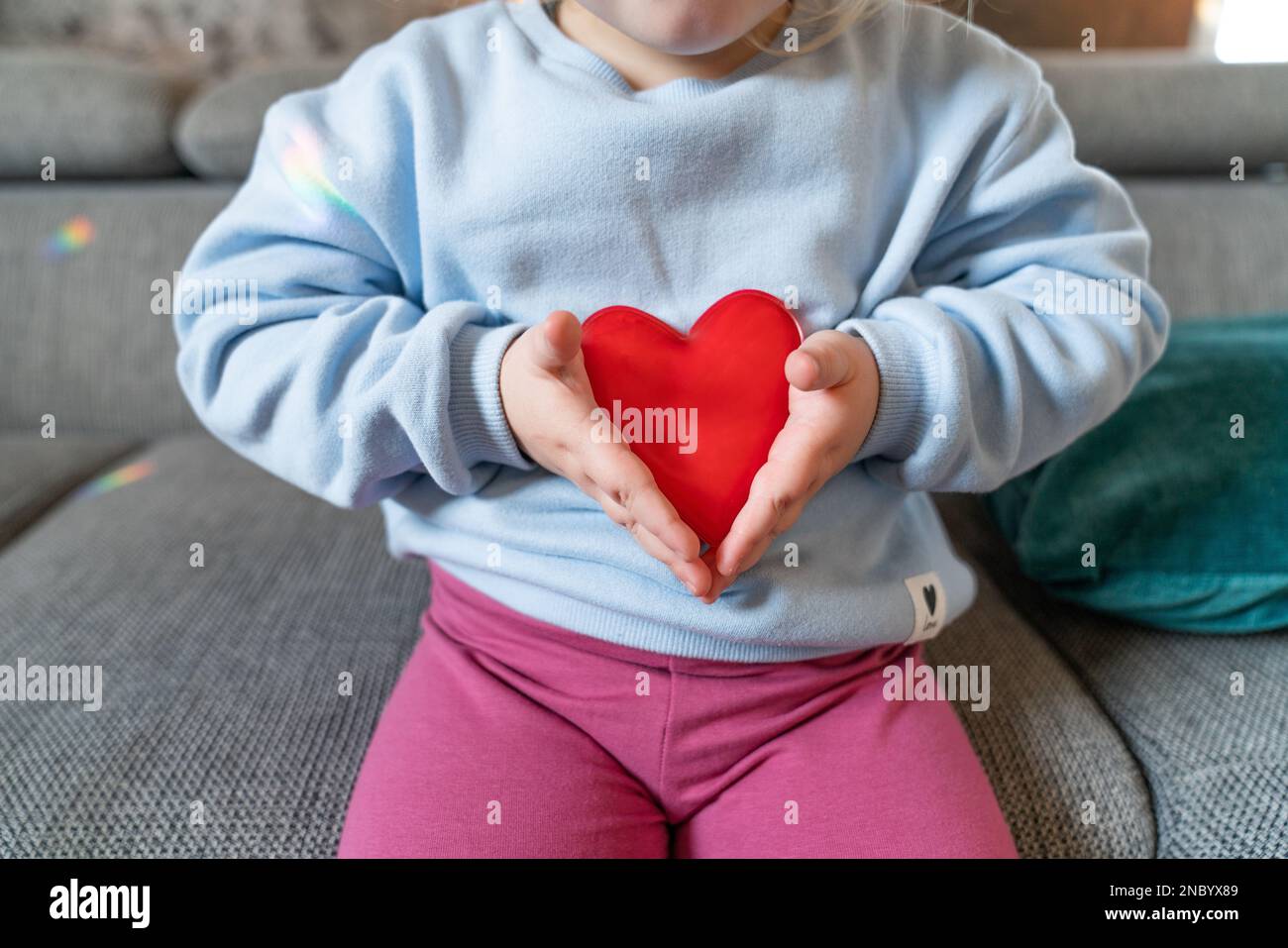 A toddler girl is holding two red hearts Stock Photo