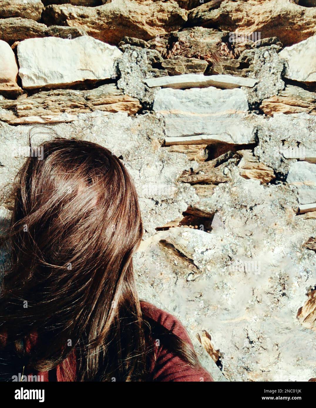 A woman stands on a rocky wall, hair covering or hiding her face Stock Photo