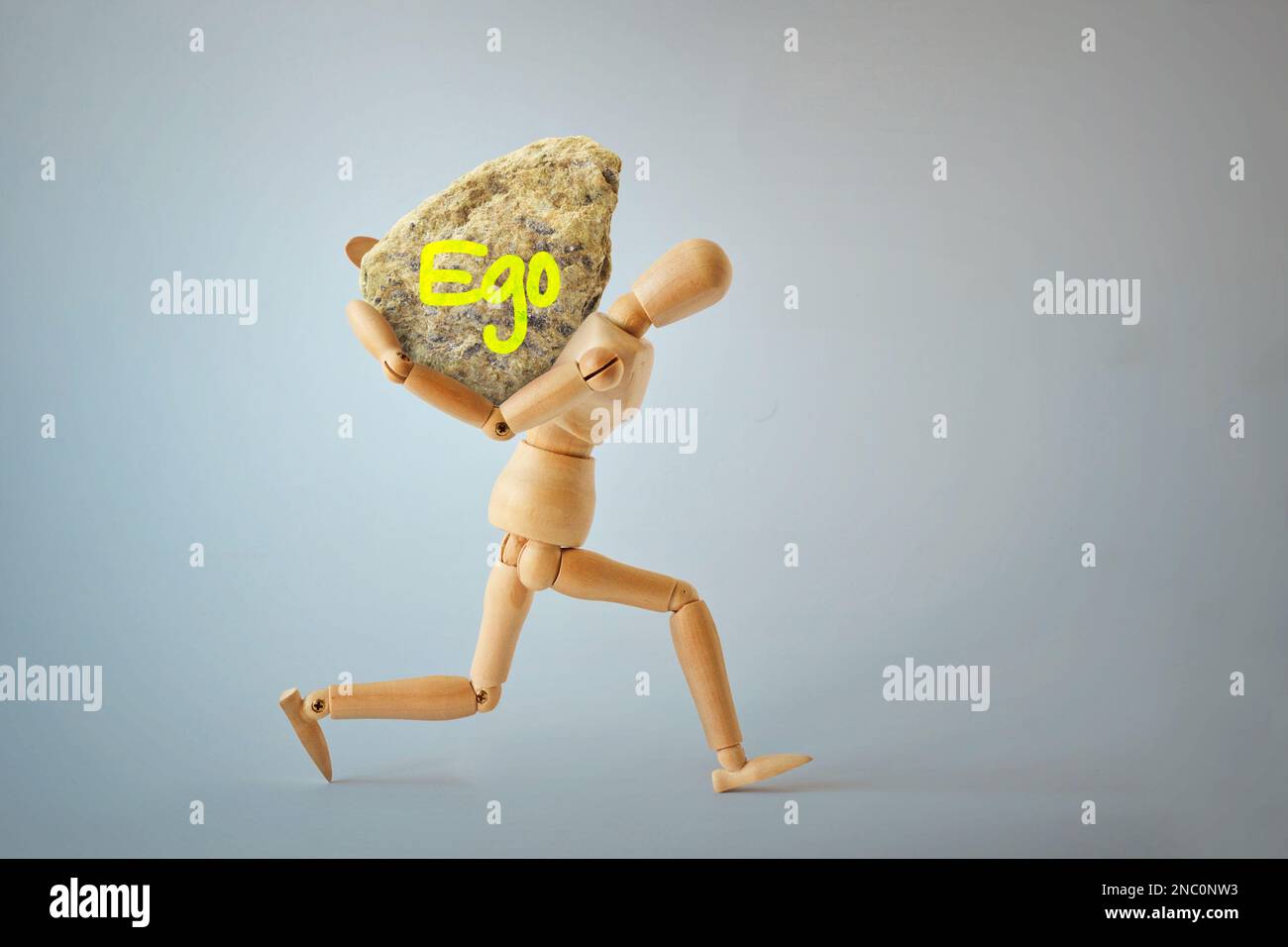 Wooden mannequin carrying heavy rock on his back - Concept of ego and emotional burden Stock Photo