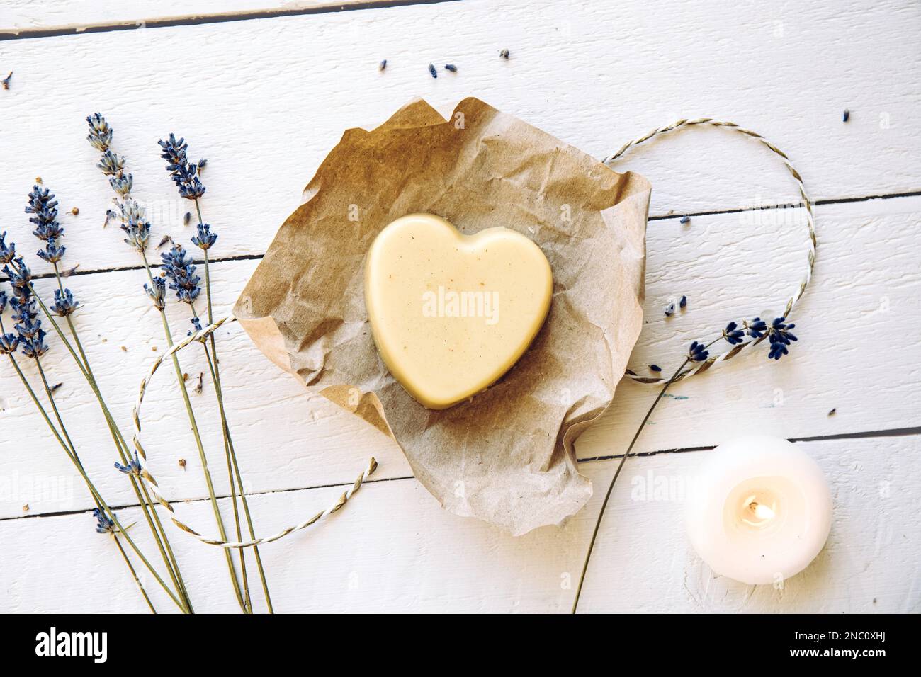 Handmade beeswax and shea butter solid moisturizing hand cream. Heart shape cream bar made of all natural ingredients. White wood board background. Stock Photo